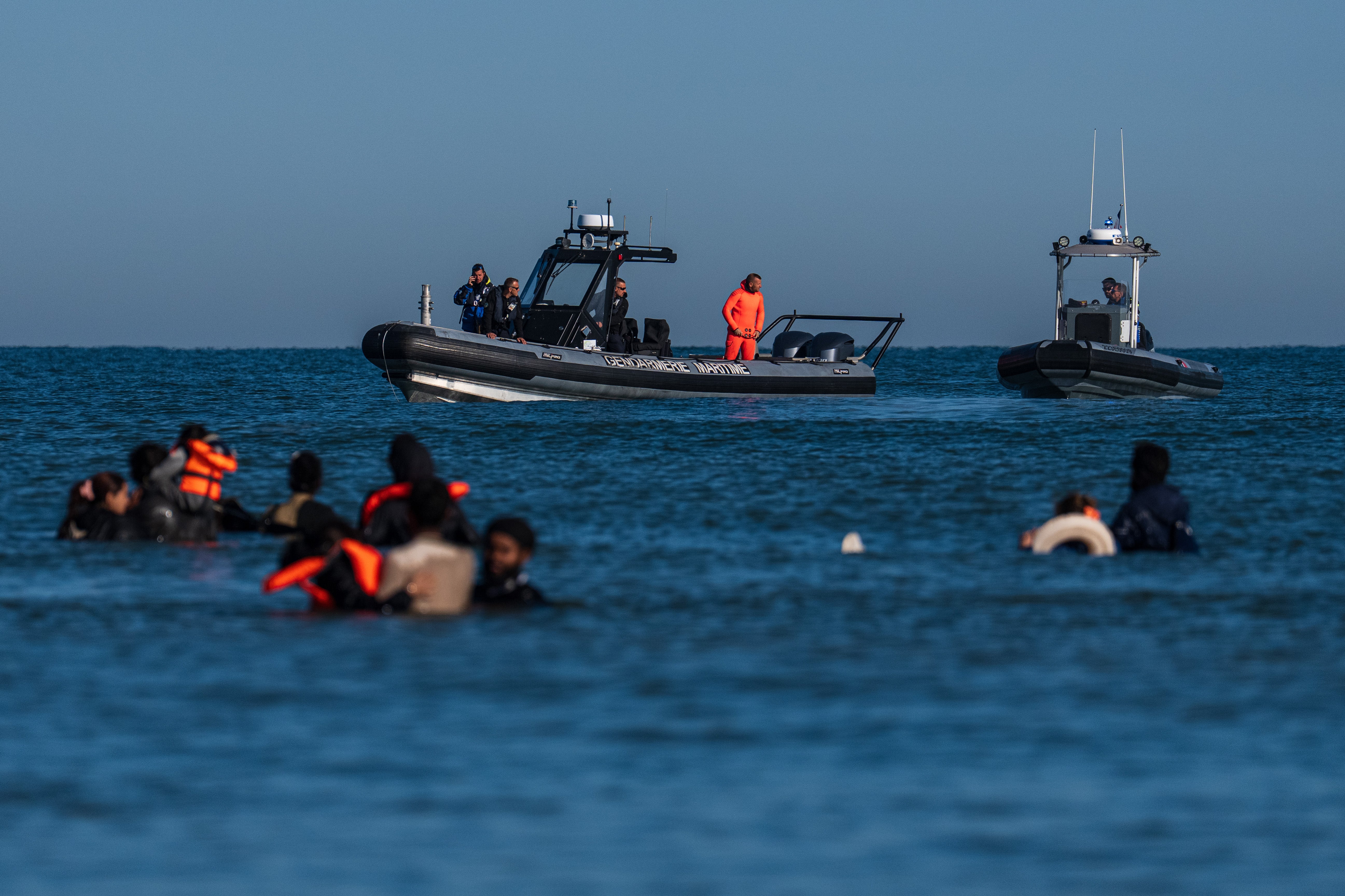French police vessels look on as migrants wade into the sea to try and board a dinghy to cross the English Channel on August 25, 2025 in Gravelines, France.