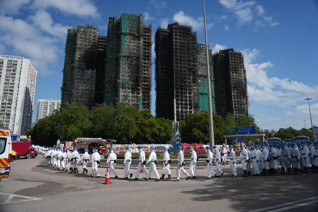 <p>Police officers from the Disaster Victim Identification Unit (DVIU), dressed in white-coloured full-body protective gear, walk past the housing blocks of Wang Fuk Court in the aftermath of the deadly November 26 fire, in Hong Kong</p>