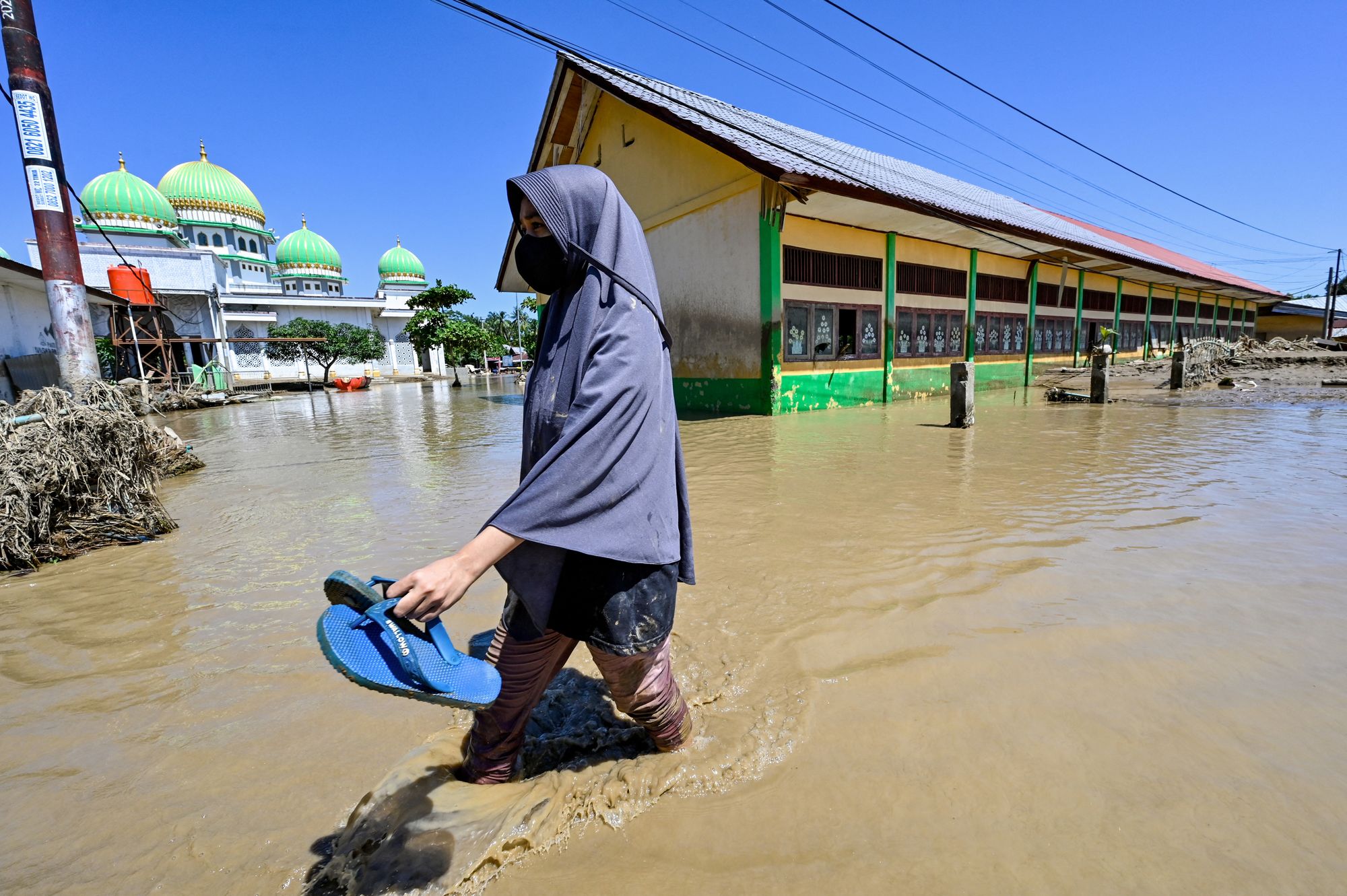 A woman walks past a mosque in a flooded area in Meureudu, Pidie Jaya district in Indonesia's Aceh province on 30 November 2025