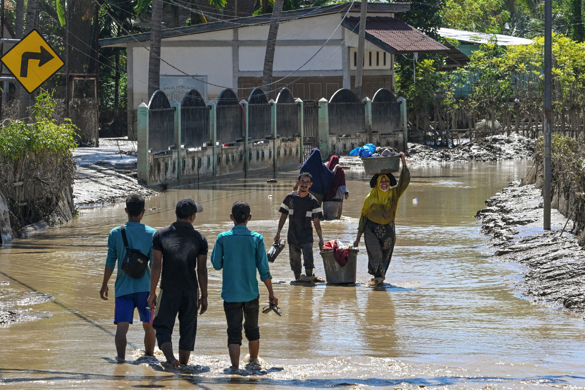 People carry their belongings as they walk in the mudflow in the aftermath of flash floods in Meureudu, Pidie Jaya district in Indonesia's Aceh province on 30 November 2025