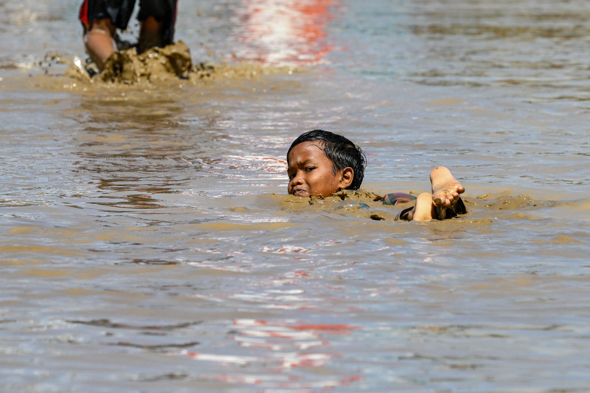 A child swims in the mudflow in the aftermath of flash floods in Meureudu, Pidie Jaya district in Indonesia's Aceh province on 30 November 2025