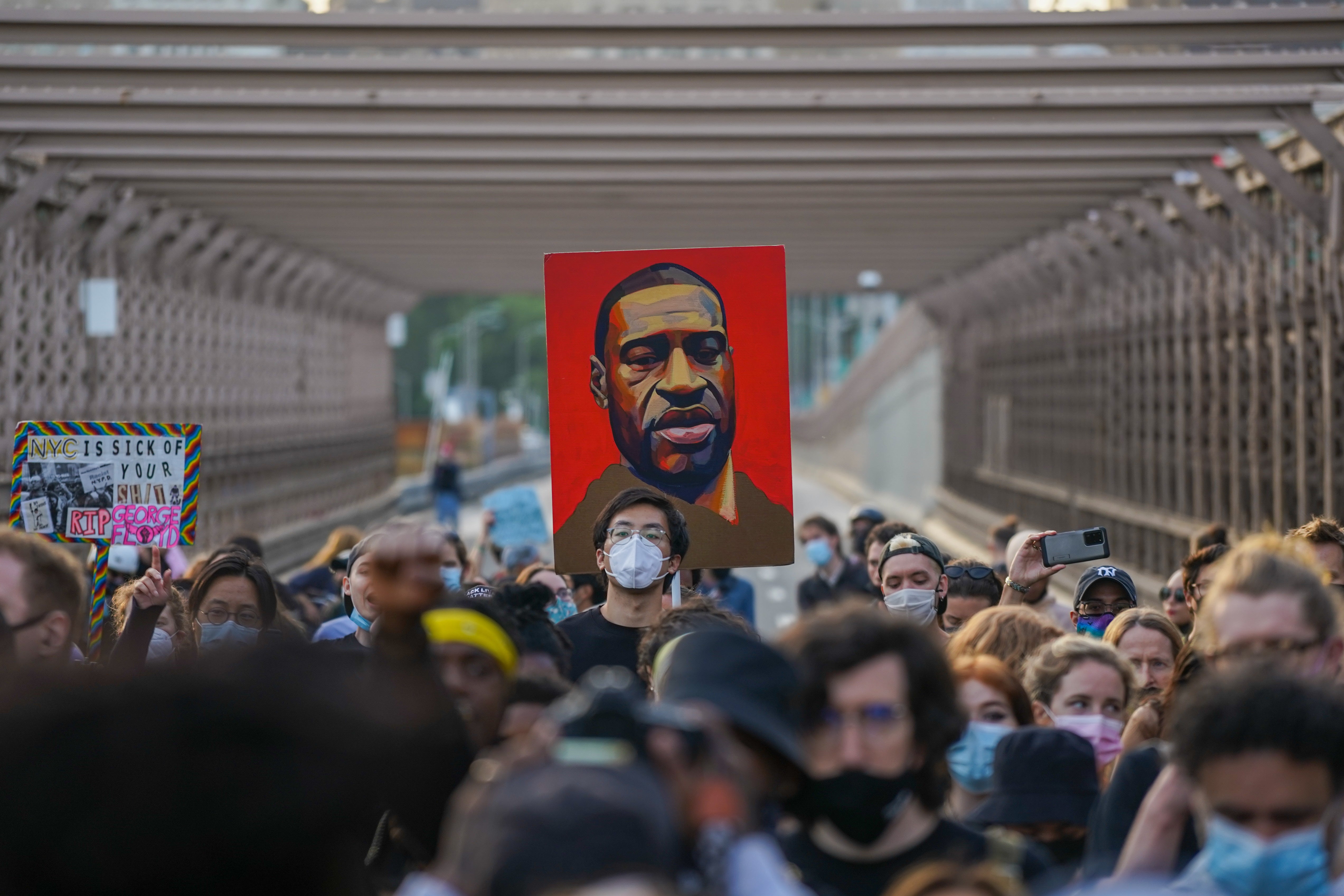 Protesters gather while holding signs, including a portrait of George Floyd. His murder sparked protests nationwide, with demonstrators advocating for racial justice and police reform. Now, the cop who killed him is asking for a new trial.