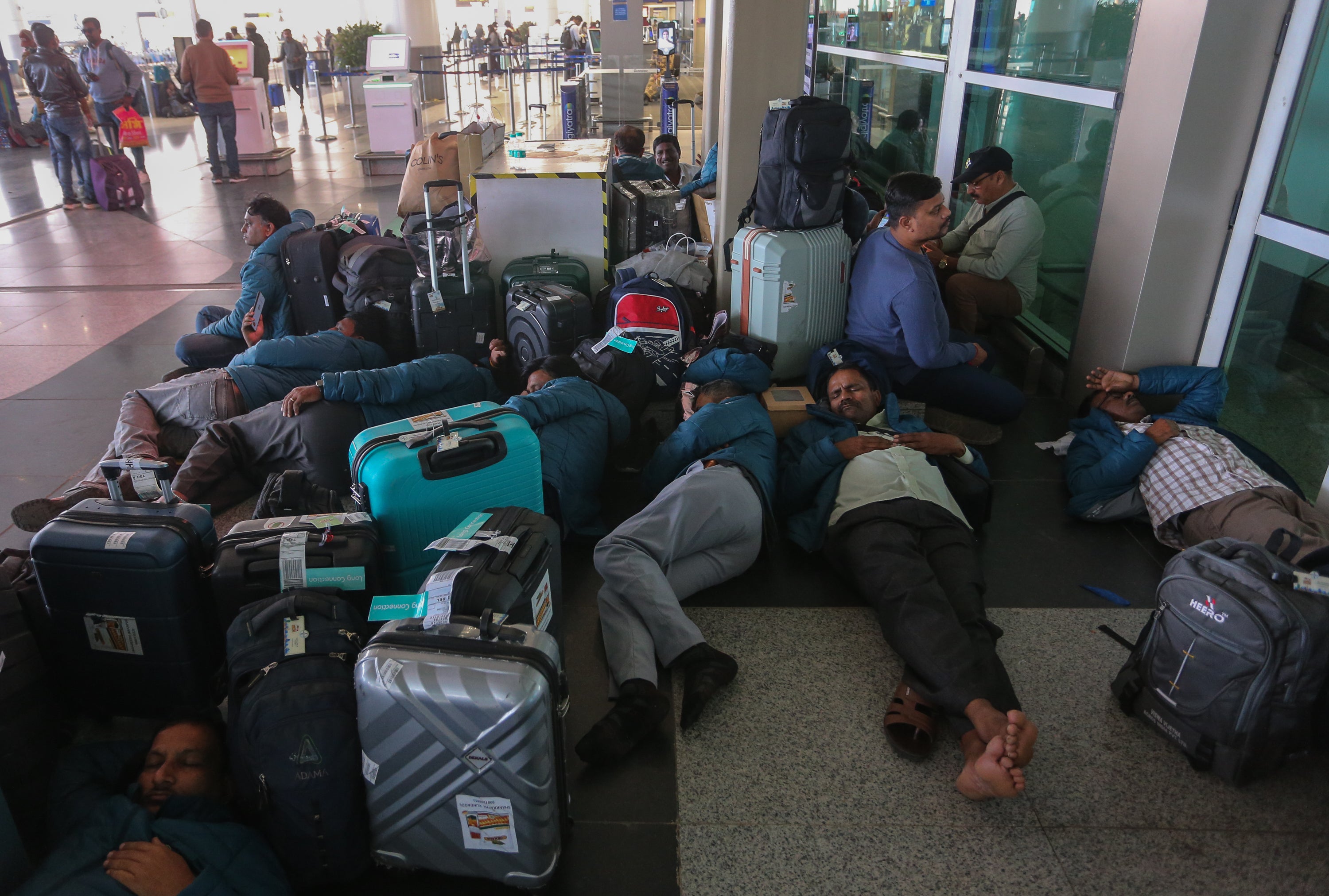 Passengers rest outside of Terminal 1 of Indira Gandhi International Airport after mass cancellation of Indigo flights on December 05, 2025 in New Delhi, India.