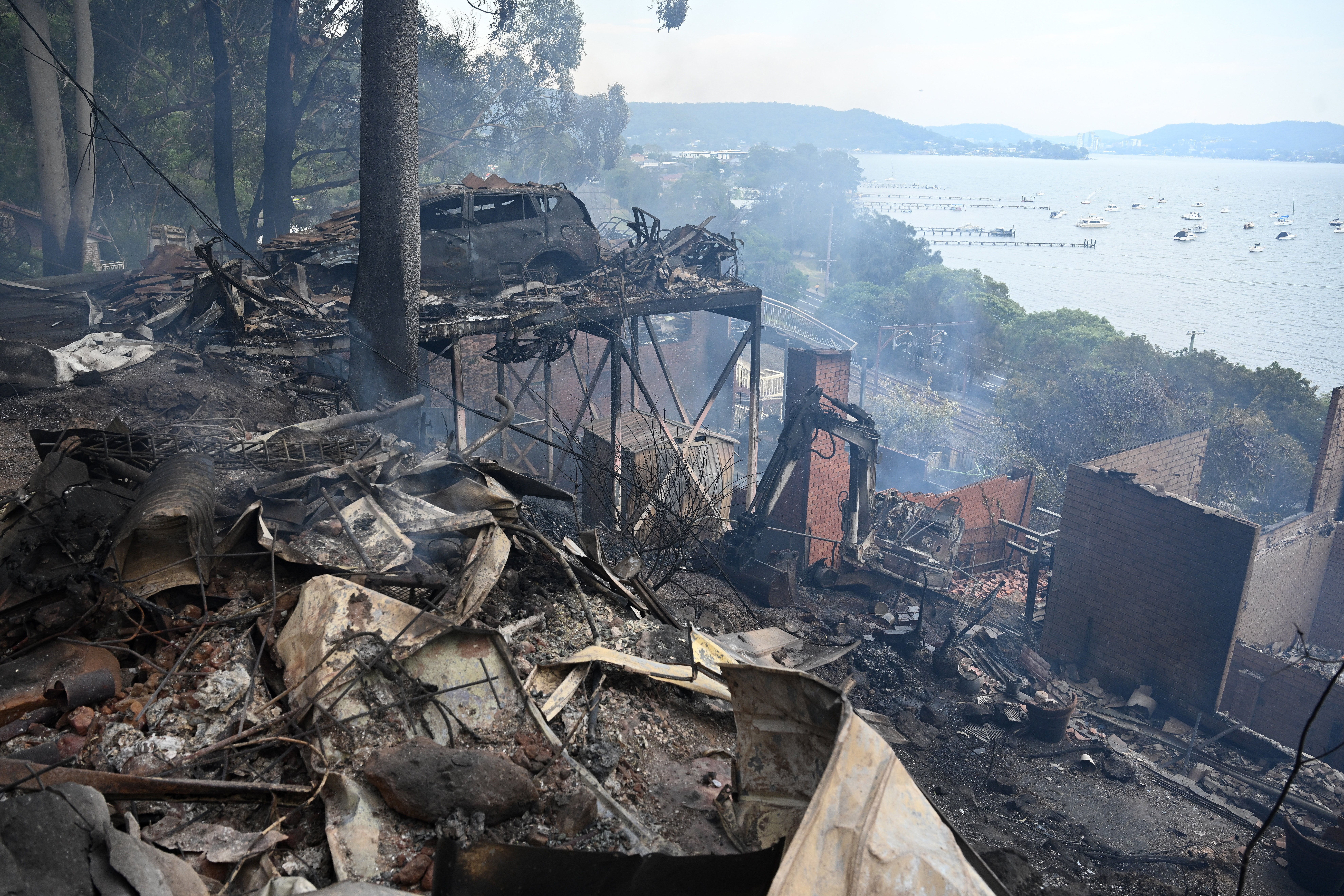Ruins of buildings and a car smolder after a wildfire destroyed houses in Koolewong, Australia