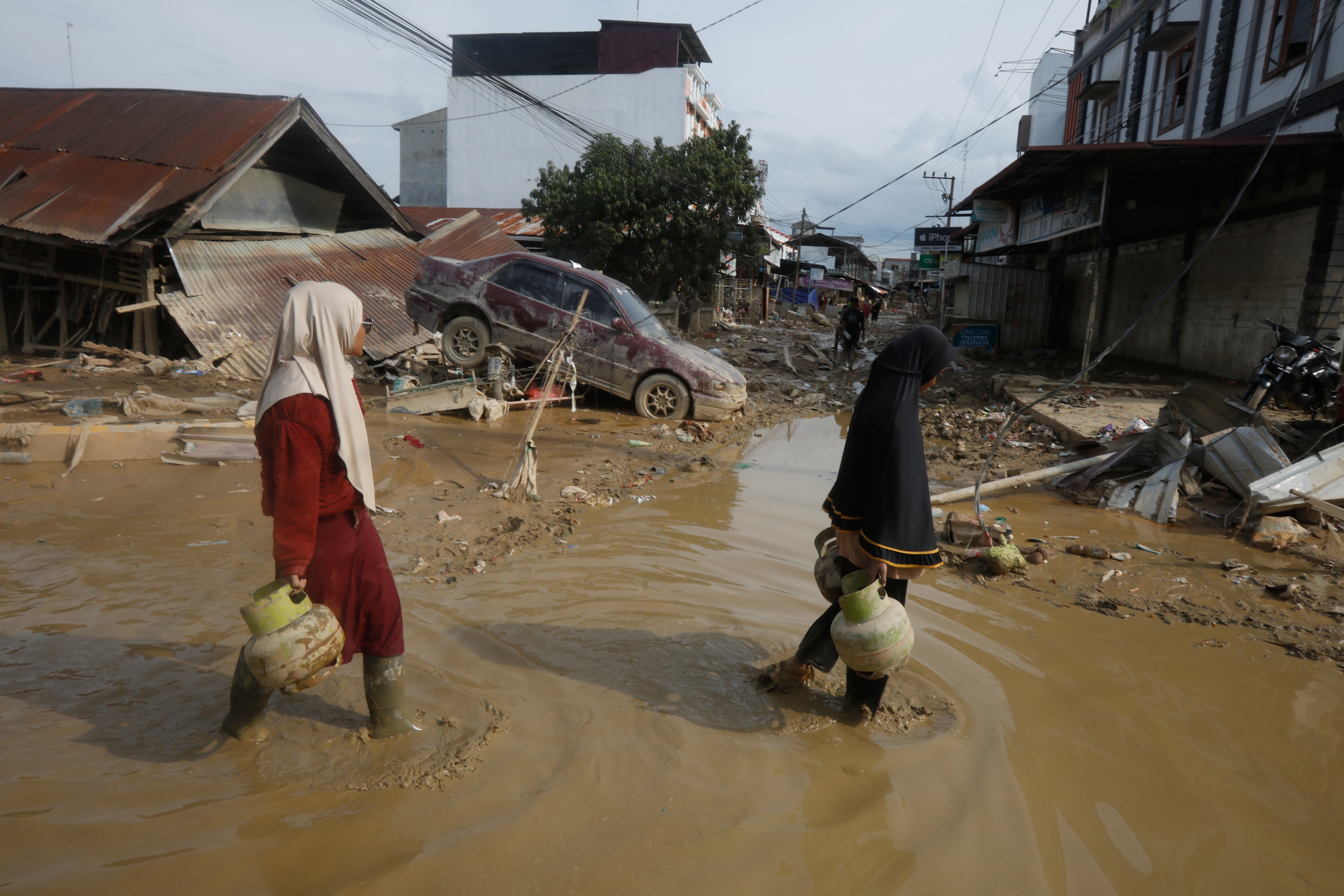 <p>Survivors walk past the wreckage of a car at an area affected by flash flooding in the aftermath of Cyclone Senyar in Aceh Tamiang, on Sumatra Island, Indonesia</p>