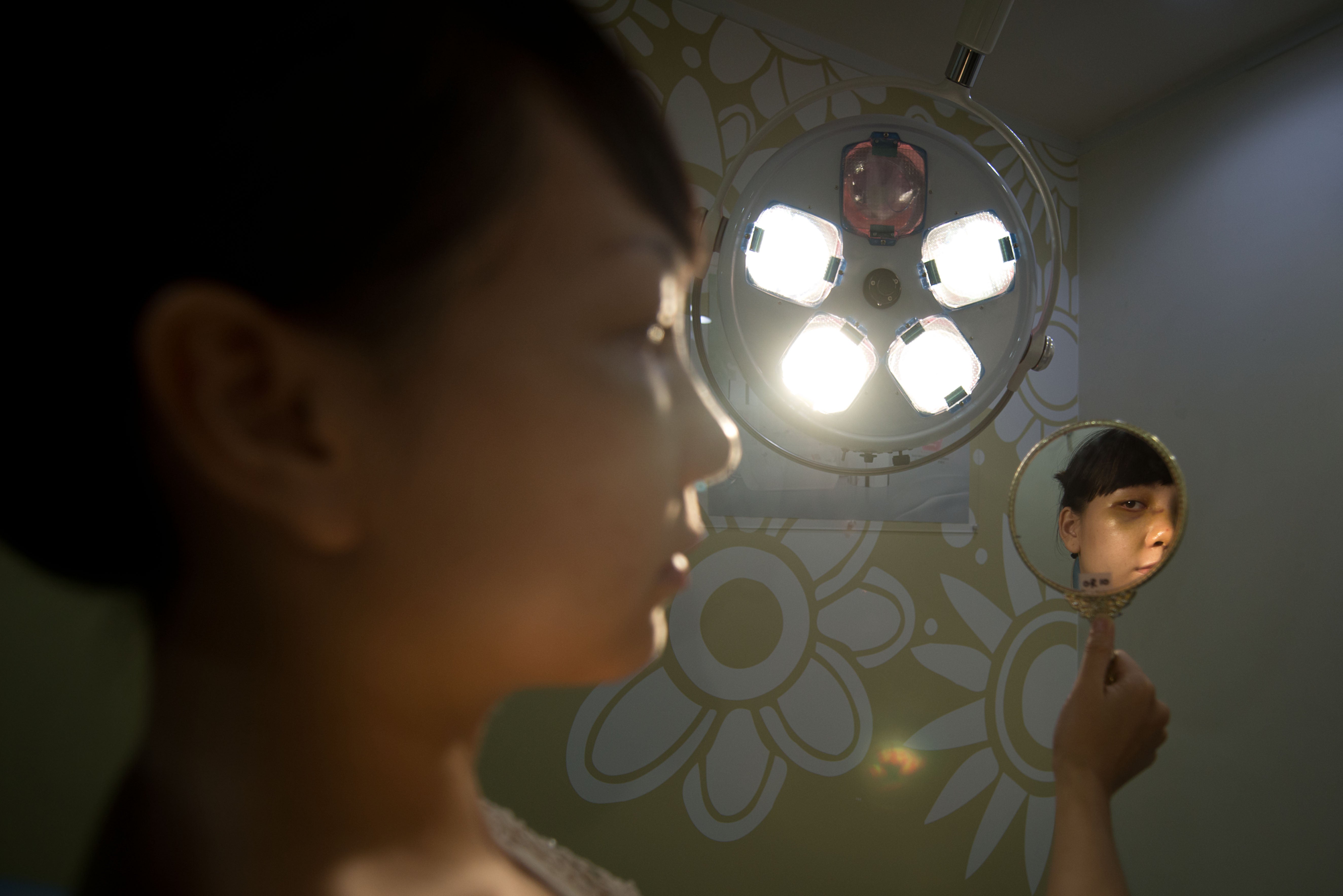 <p>FILE: A Vietnamese-American patient checks her appearance four days after undergoing a cosmetic rhinoplasty and eye procedures in Seoul</p>