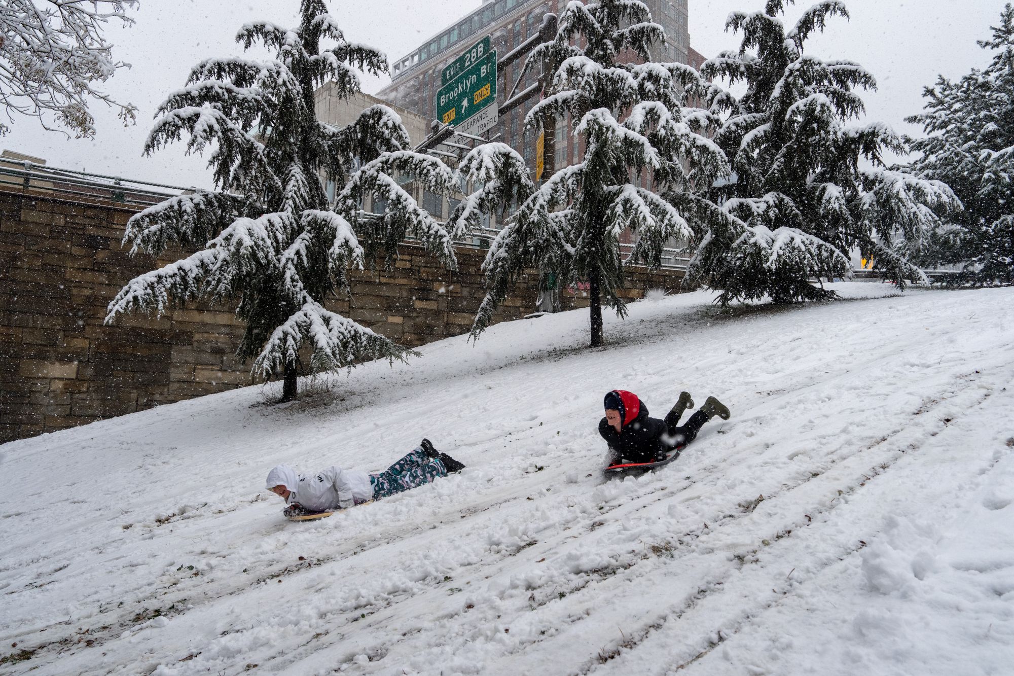 Two people sled in the snow next to the Brooklyn-Queens Expressway