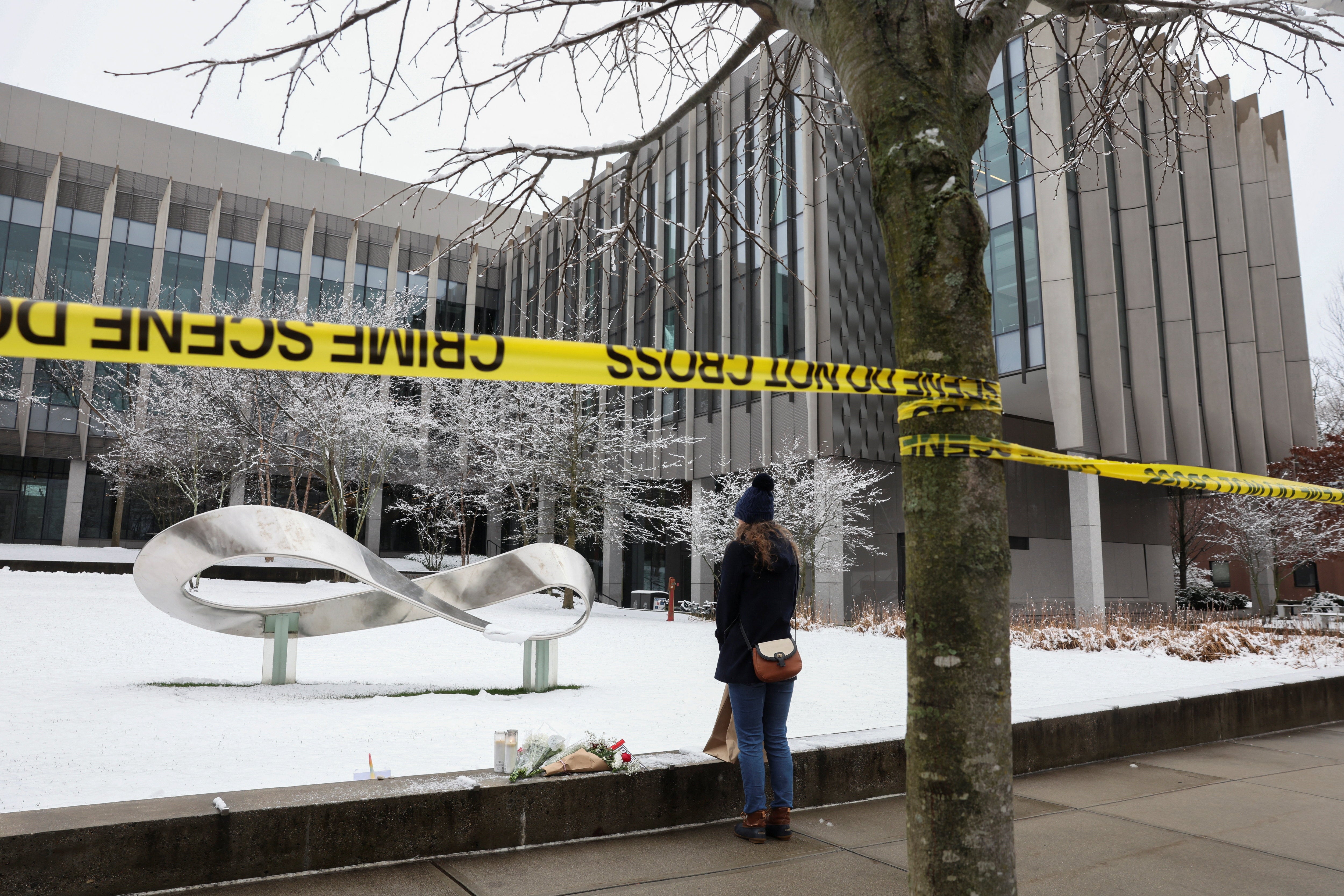 A woman leaves flowers at the scene of a mass shooting at Brown University the morning after two students were killed and nine other wounded in a mass shooting on the Ivy League campus