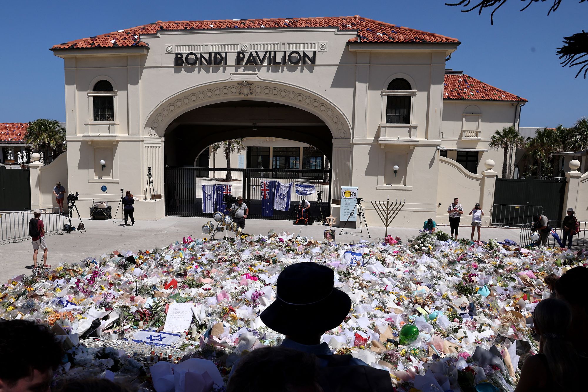 Mourners stand near tributes piled together at the front of the Bondi Pavilion, in memory of the victims of the Bondi Beach shooting, in Sydney on 17 December 2025
