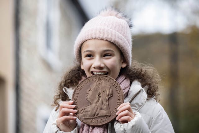 A girl takes a bite out of a chocolate coin as part of a collection of historical chocolate coins being unveiled to celebrate the opening of Cash Access UK’s 200th banking hub in Billericay, Essex (Matt Alexander/PA Media Assignments)