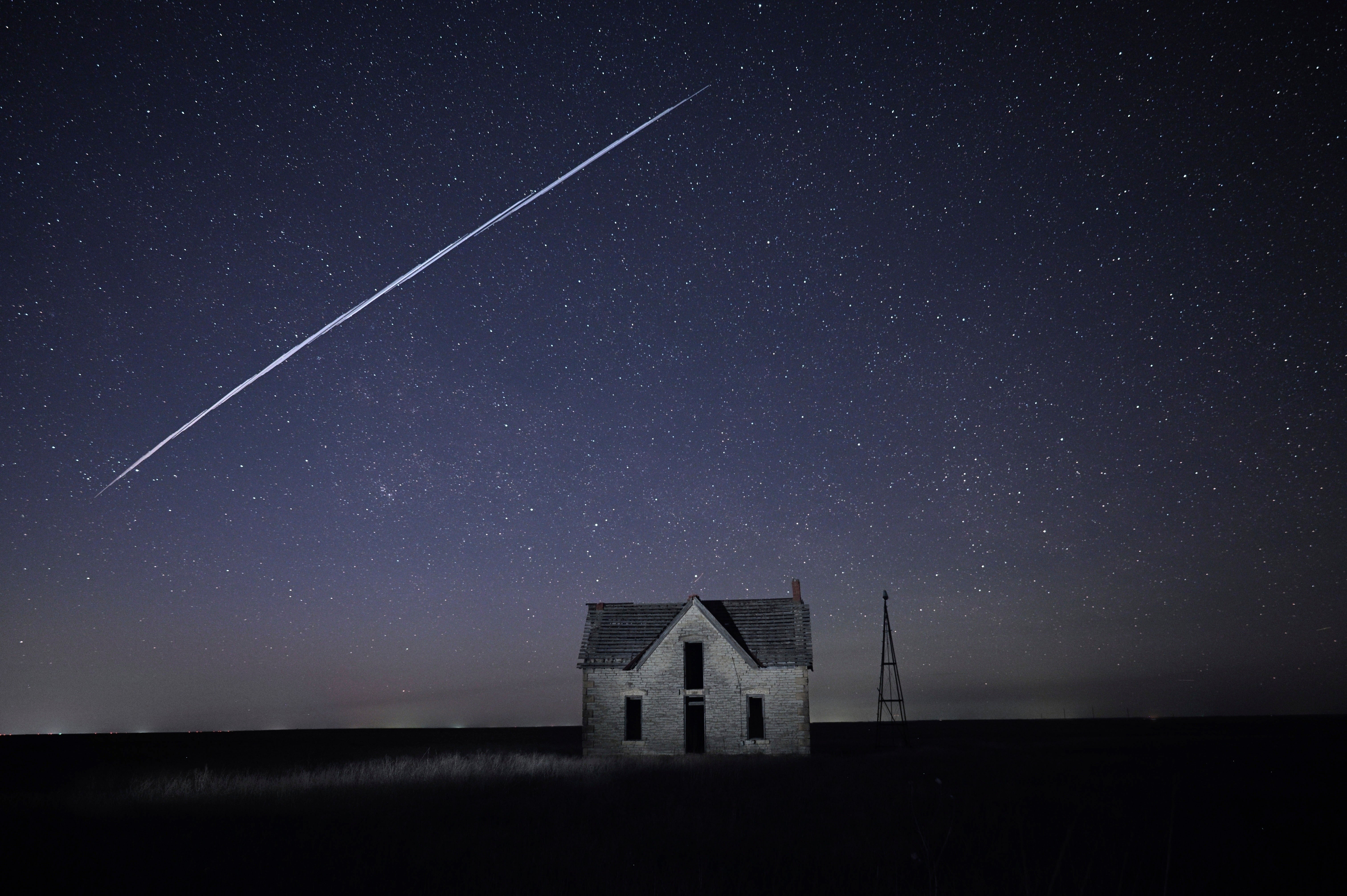 In this long exposure photo, a string of SpaceX StarLink satellites passes over an old stone house.