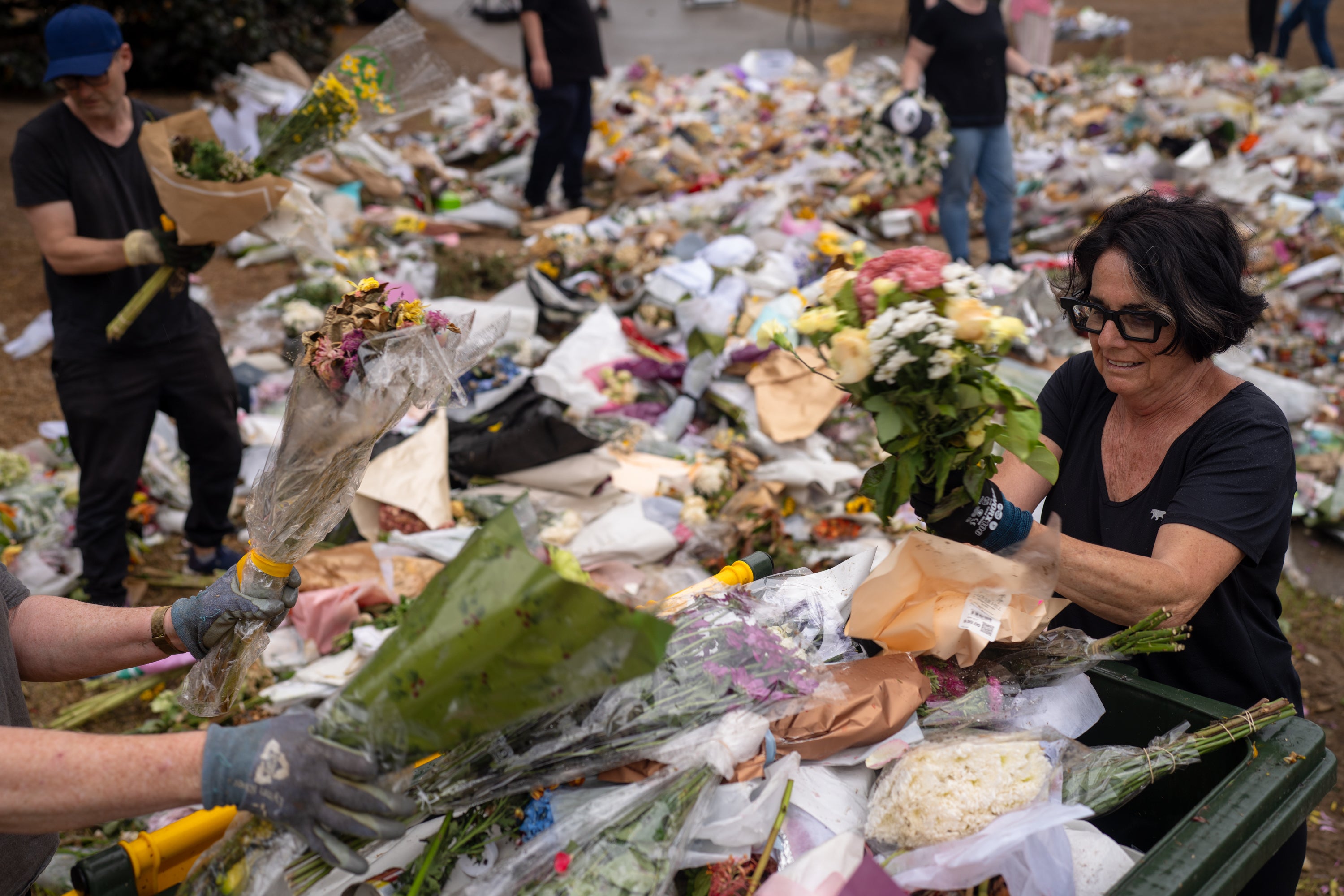 People help clear flowers and notes, honoring the victims and survivors of the Bondi Beach mass shooting, at Bondi Pavilion on 22 December 2025 in Sydney, Australia