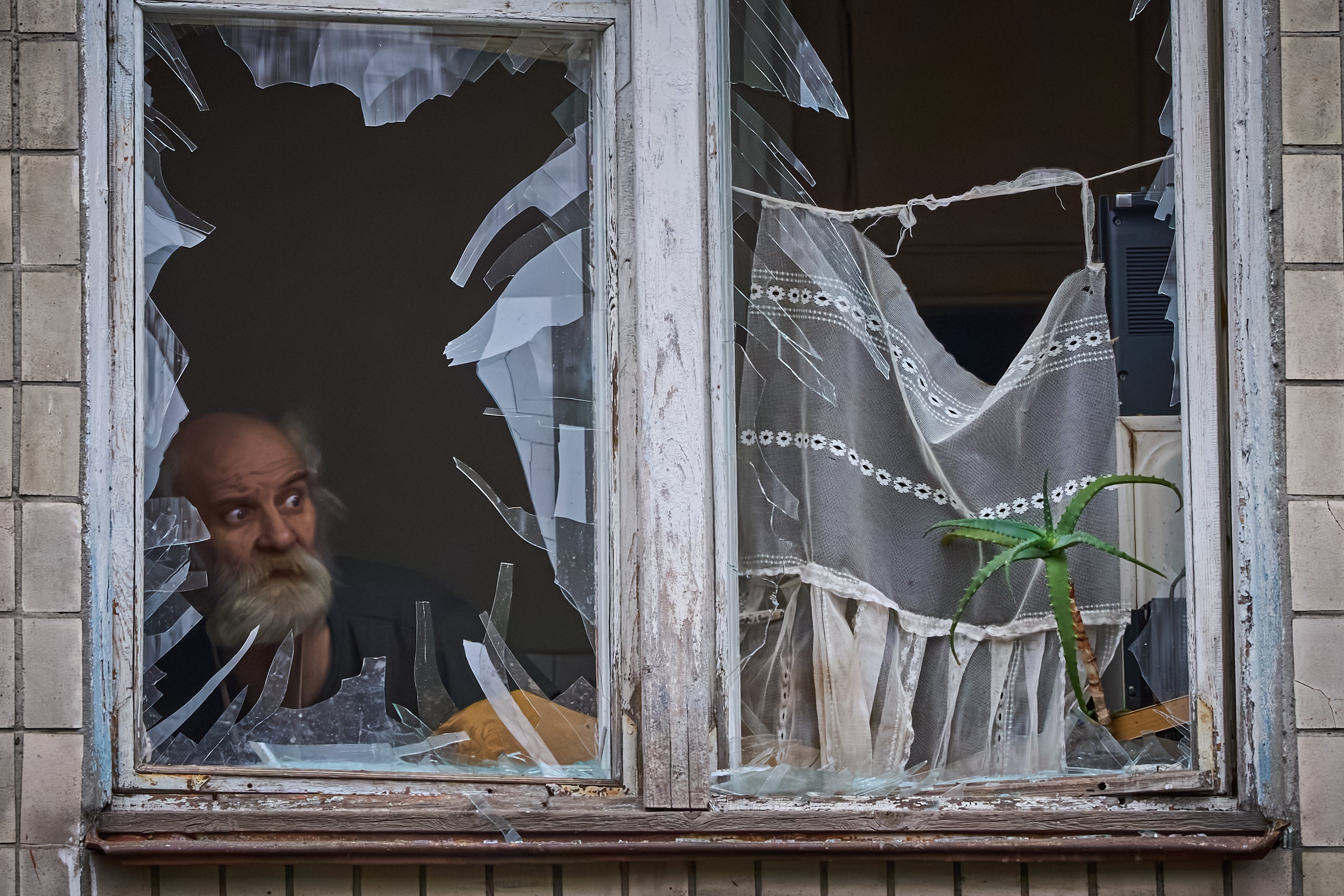 An elderly man looks out of his broken window as an apartment building was hit by a Russian drone during an aerial attack in Kyiv, Ukraine, Tuesday, 23 December