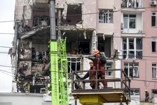 Workers repare cables in front of a damaged residential building following Russian drones and missiles attack in Kyiv, on December 27, 2025