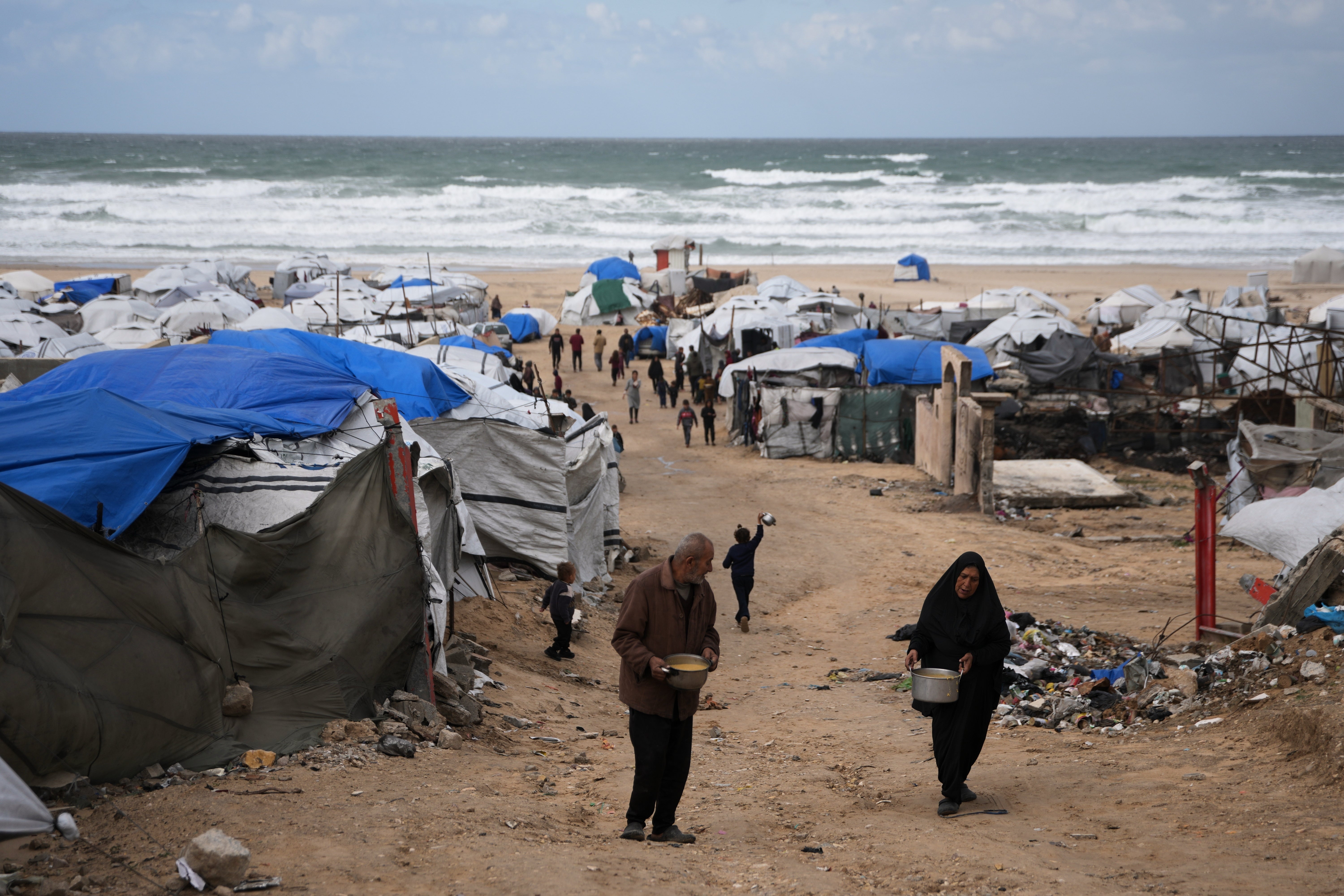 Palestinians receive donated food at a temporary camp for displaced people, on the beach near the port of Gaza City, Sunday, Dec. 28, 2025. (AP Photo/Jehad Alshrafi)