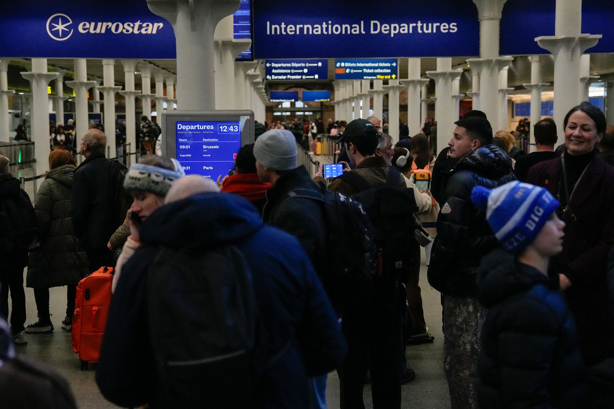Travellers at the departures hall at St. Pancras station in London look on at the departures board