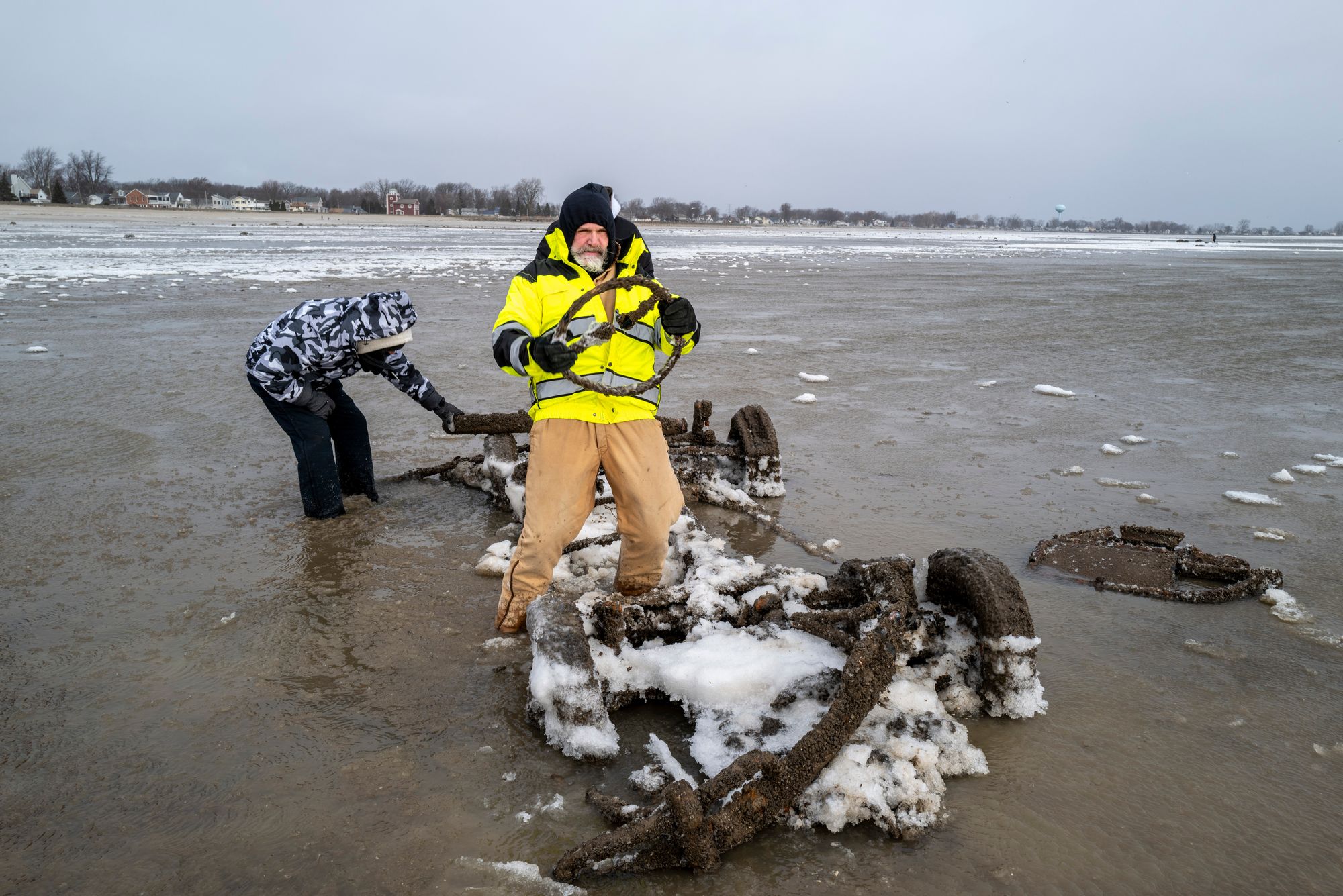 Neil Wakeman, a Luna Pier city council member, holds up a steering wheel as he and friends look over a car that is normally submerged in roughly eight feet of water in Luna Pier, Mich., on Dec. 29, 2025