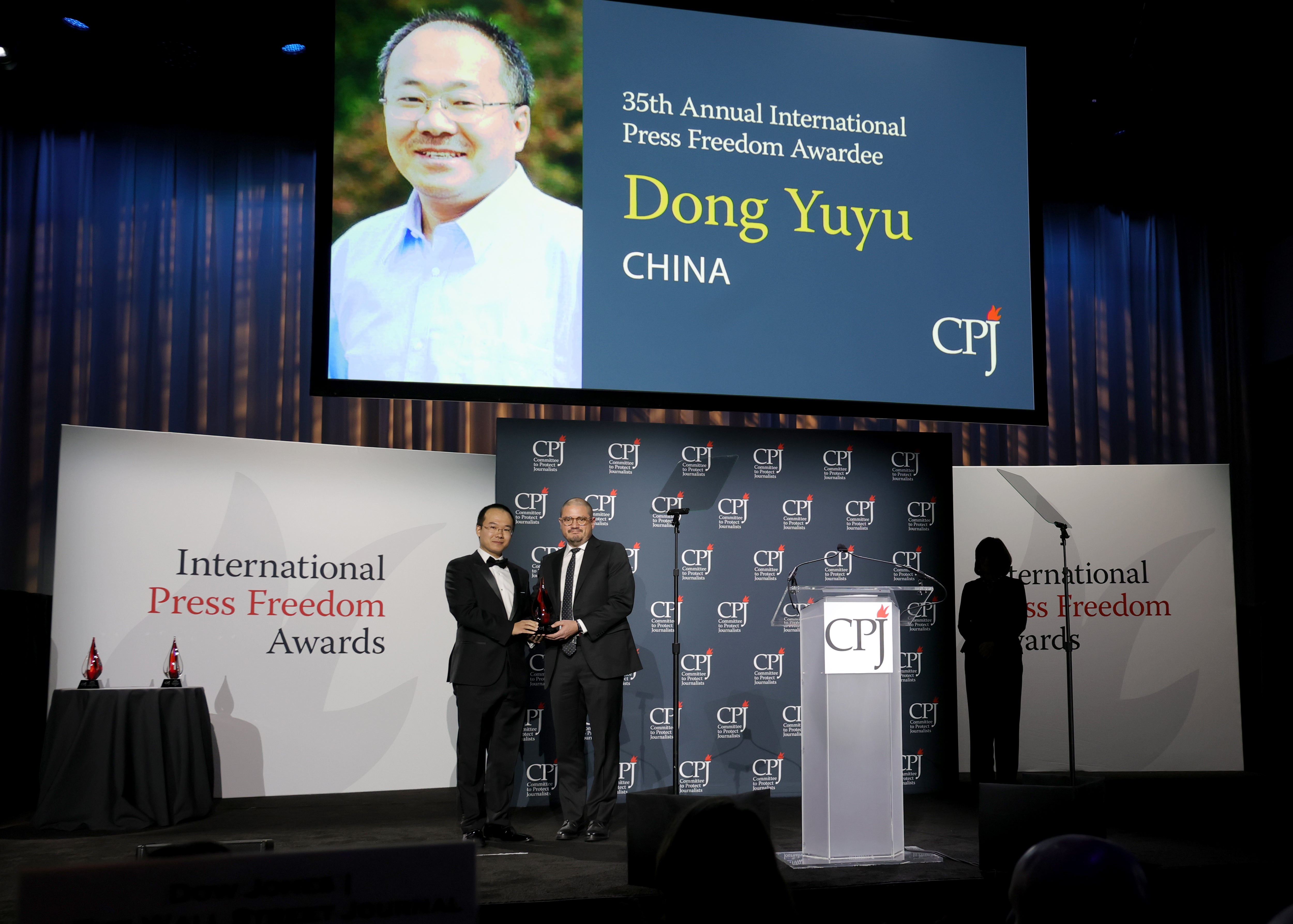Dong Yifu accepts an award from Juan Arredondo onstage during the 2025 CPJ International Press Freedom Awards at The Glasshouse on November 20, 2025 in New York City