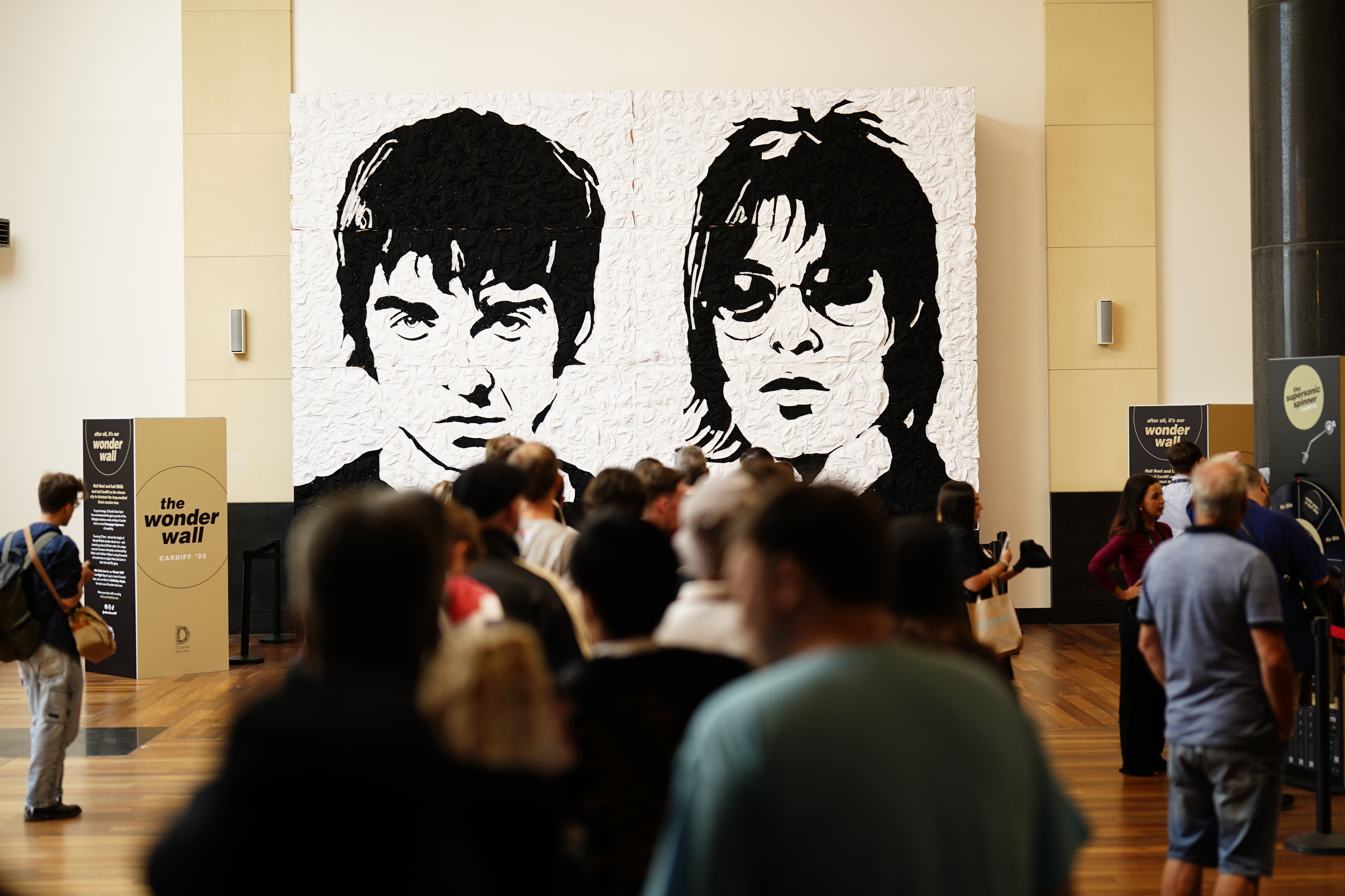 Oasis fans take photos in front of the Wonder Wall – a mural made out of 3,000 black and white bucket hats depicting Liam and Noel Gallagher – in Cardiff, ahead of the first show in the band’s long-awaited reunion tour (Jordan Pettitt/PA)