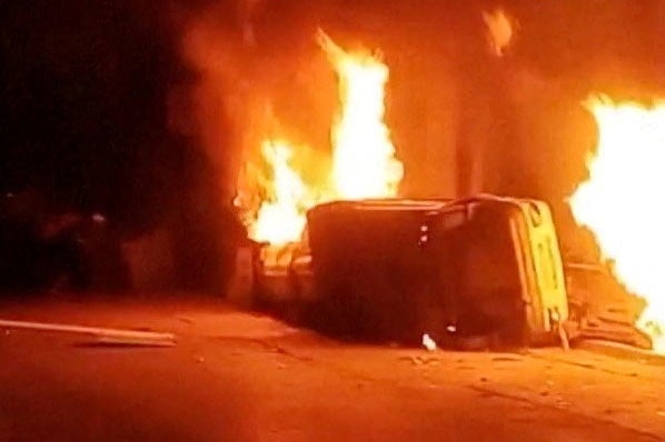 An overturned car and multiple fires burn as protesters chant outside a police station