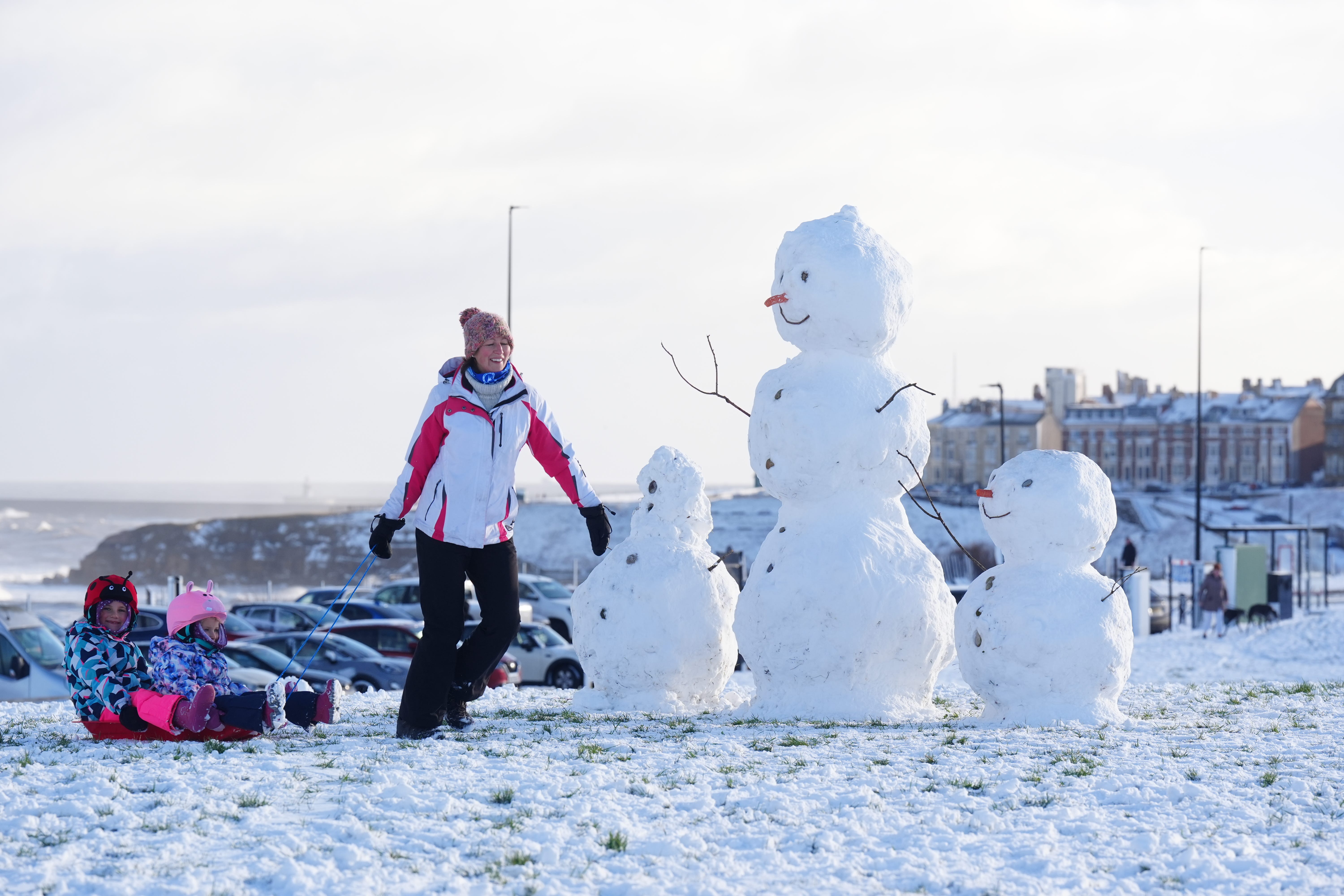 <p>A woman pulls along two children on a sledge by snowmen at Tynemouth </p>