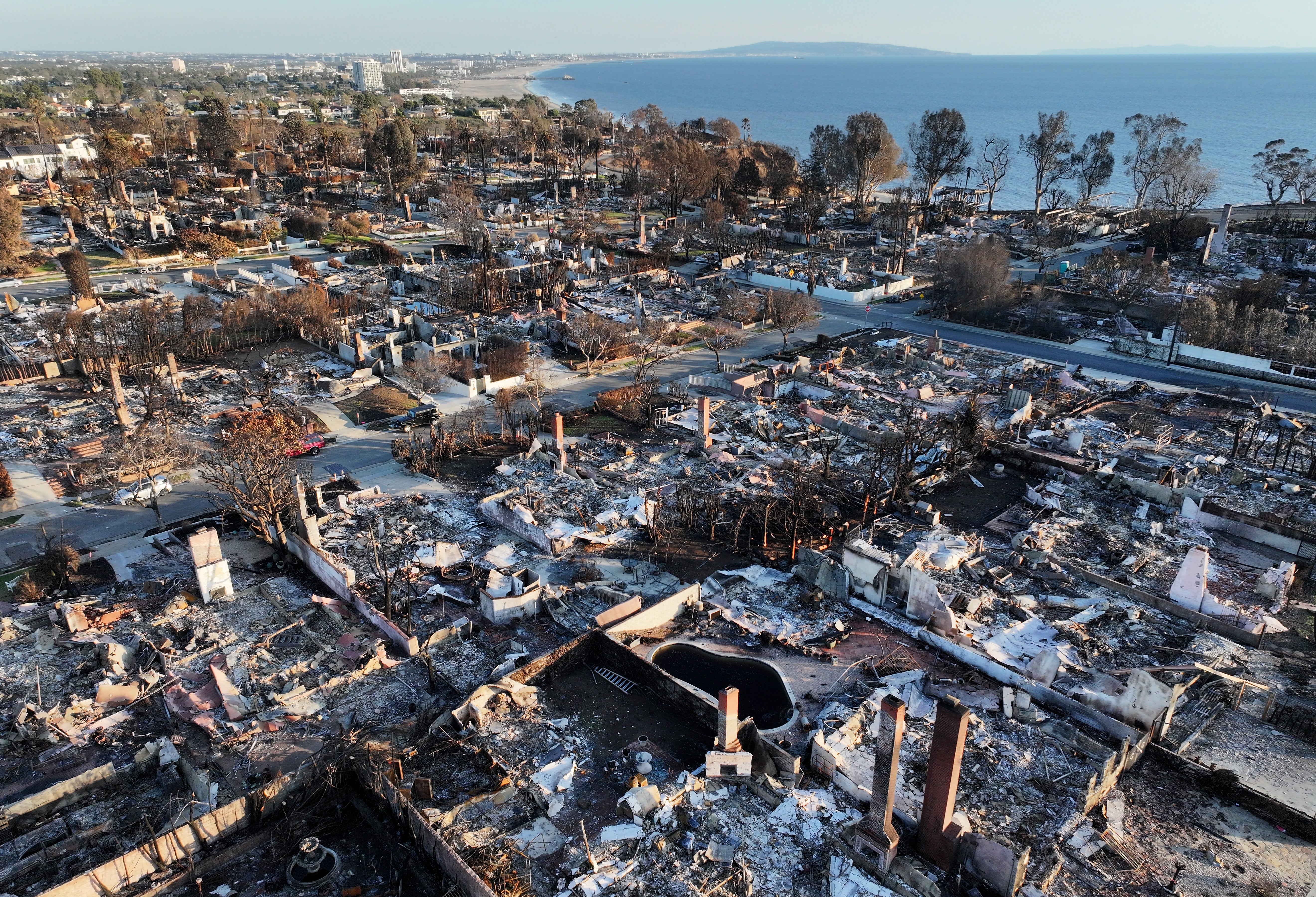 An aerial view shows homes destroyed in the Palisades Fire with the Pacific Ocean in the distance on January 27, 2025 in Pacific Palisades, California