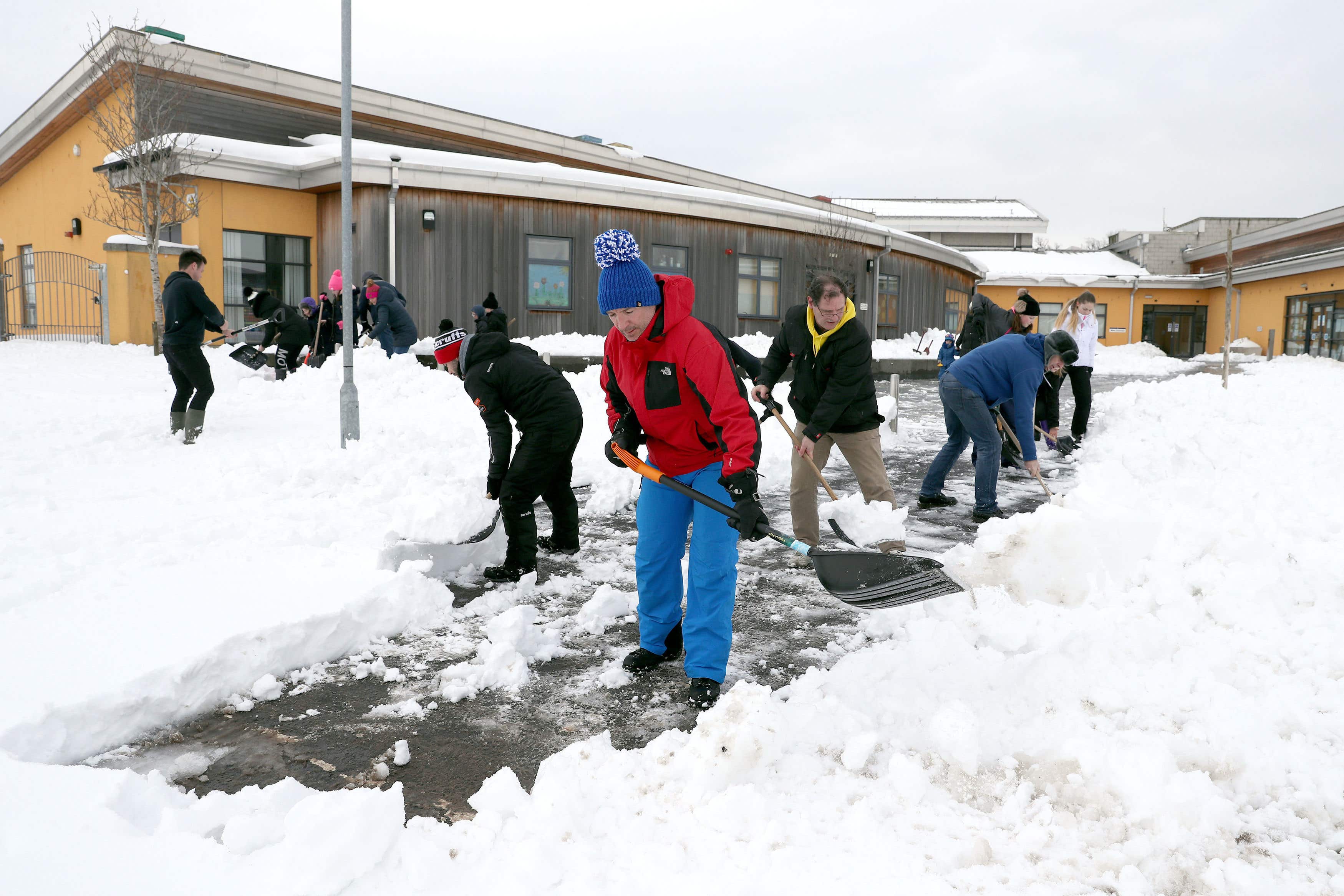 Hundreds of schools across the country have closed due to snow. Pictured, the community clears snow from outside a school
