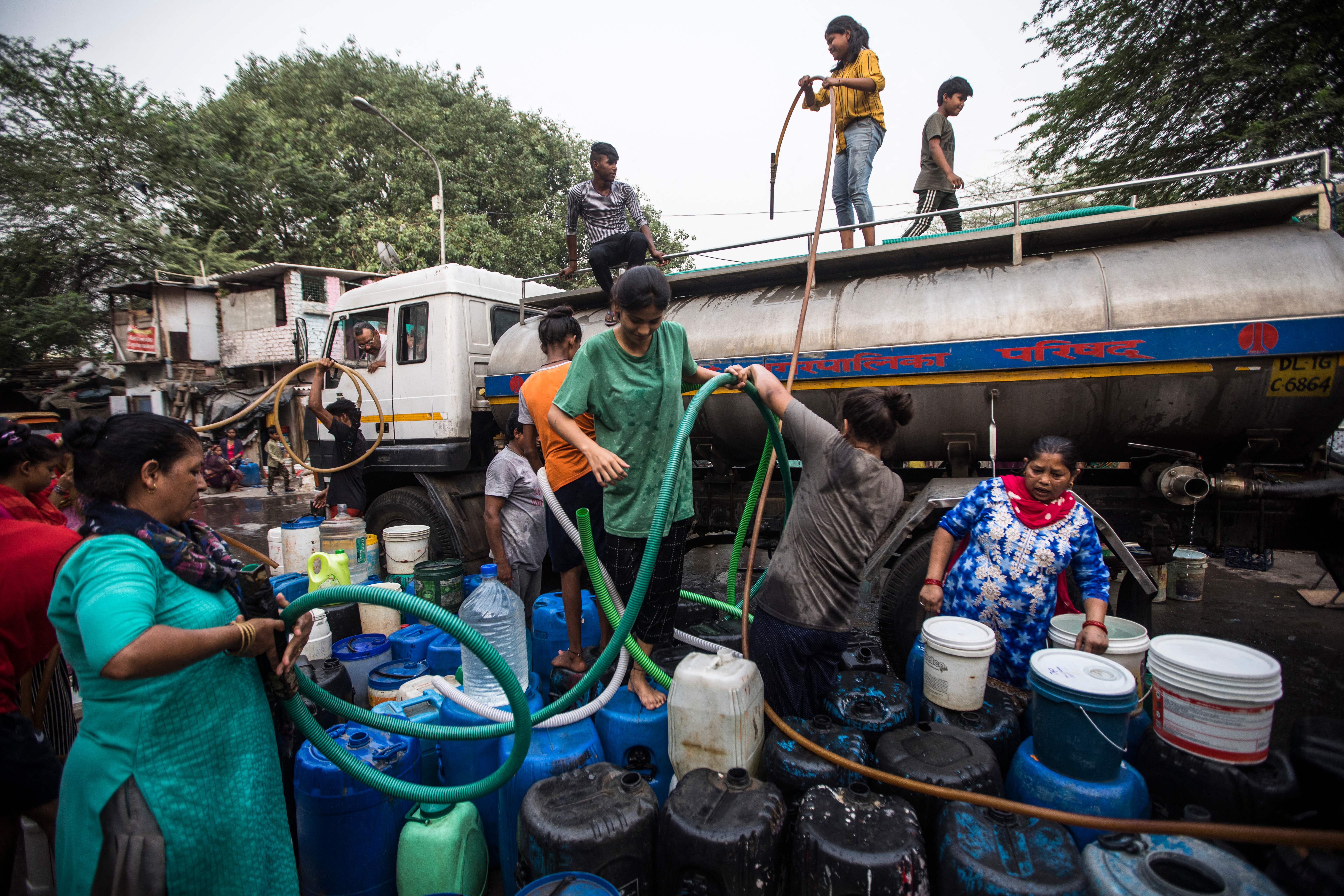 <p>Residents use hoses to collect drinking water from a tanker truck in Delhi</p>