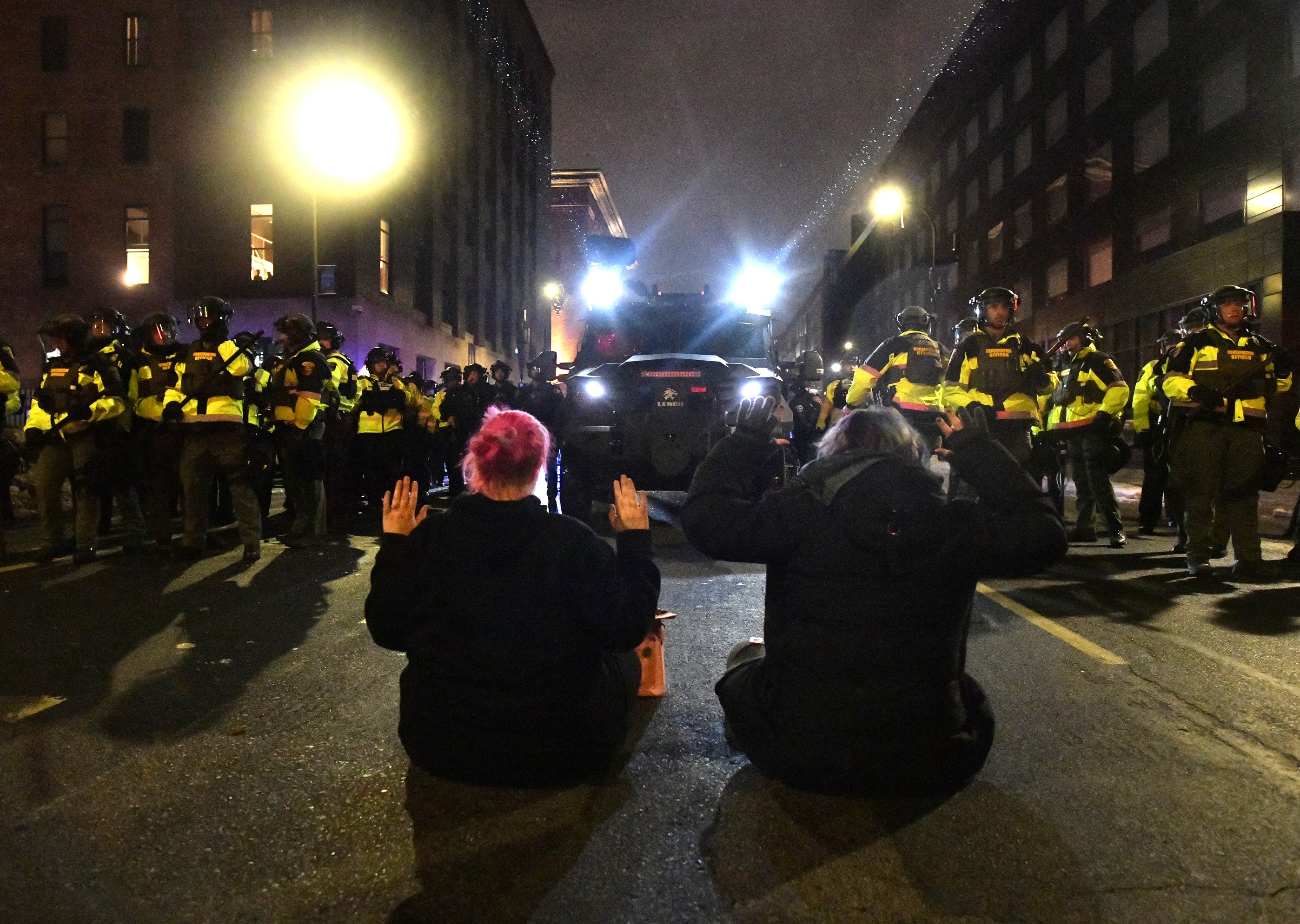 Two protesters sit on the road in front of Minnesota Conservation Officers