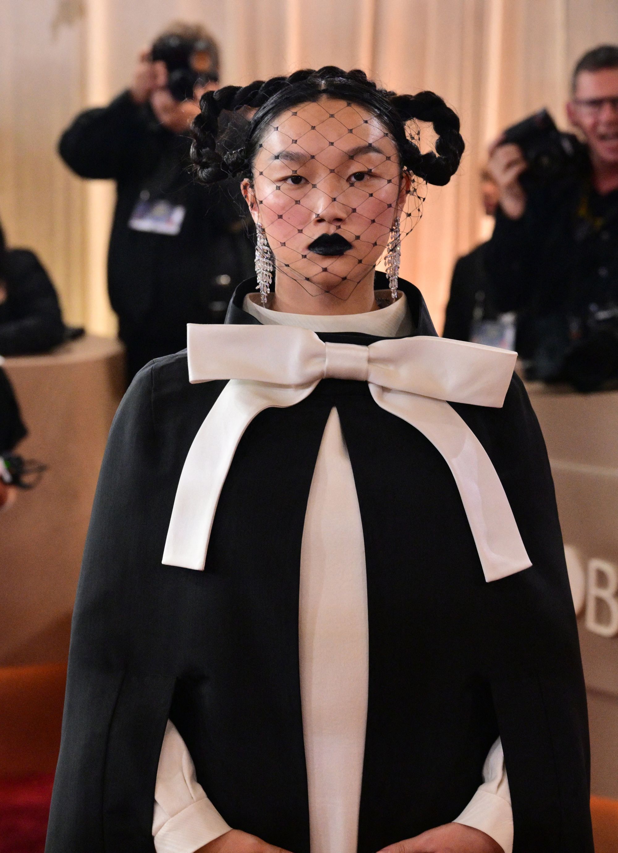 Her hair was braided and looped on either side of her head, and she wore a sheer lace face covering over black lipstick, creating a drama-filled look
