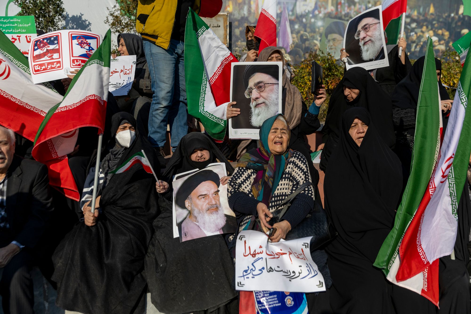 People hold placards and wave flags during a pro-government demonstration on 12 January 2026 in Tehran, Iran