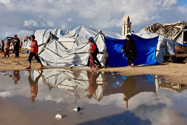 <p>Displaced Palestinians walk past a large pool of rainwater accumulated near tent shelters as the region experiences harsh winter conditions in Gaza</p>