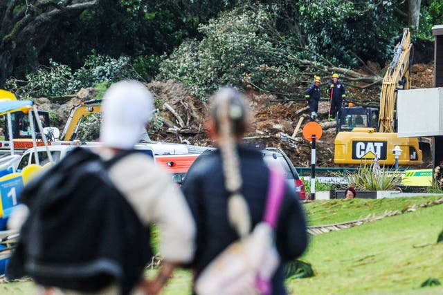 <p>A couple looks at a landslide while a search is underway by local emergency services for missing people at Mount Maunganui in Tauranga</p>