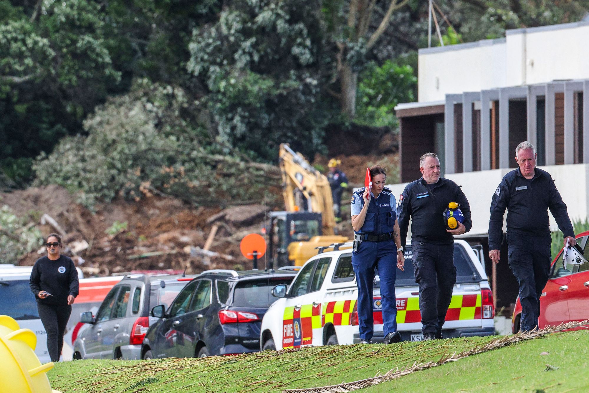 Police and officials walk following a landslide while a search is underway by local emergency services for missing people at Mount Maunganui in Tauranga
