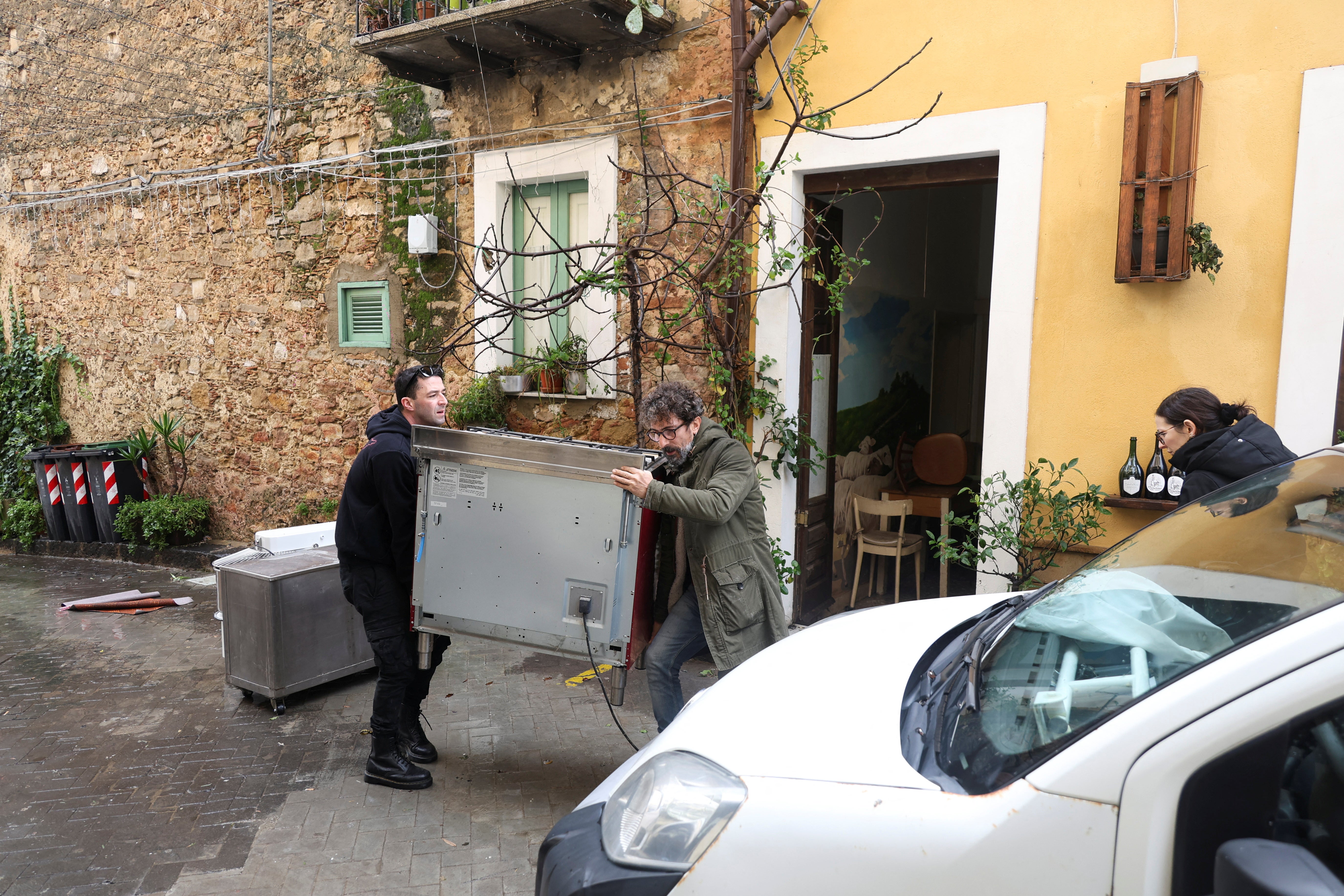 <p>Toni Rinnone (C) and a man carry a stove as residents scramble to remove belongings and mementos from homes in high-risk areas following a landslide in Niscemi, Sicily</p>