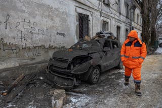 A municipal worker walks past a burned-out car near a damaged residential building on Wednesday