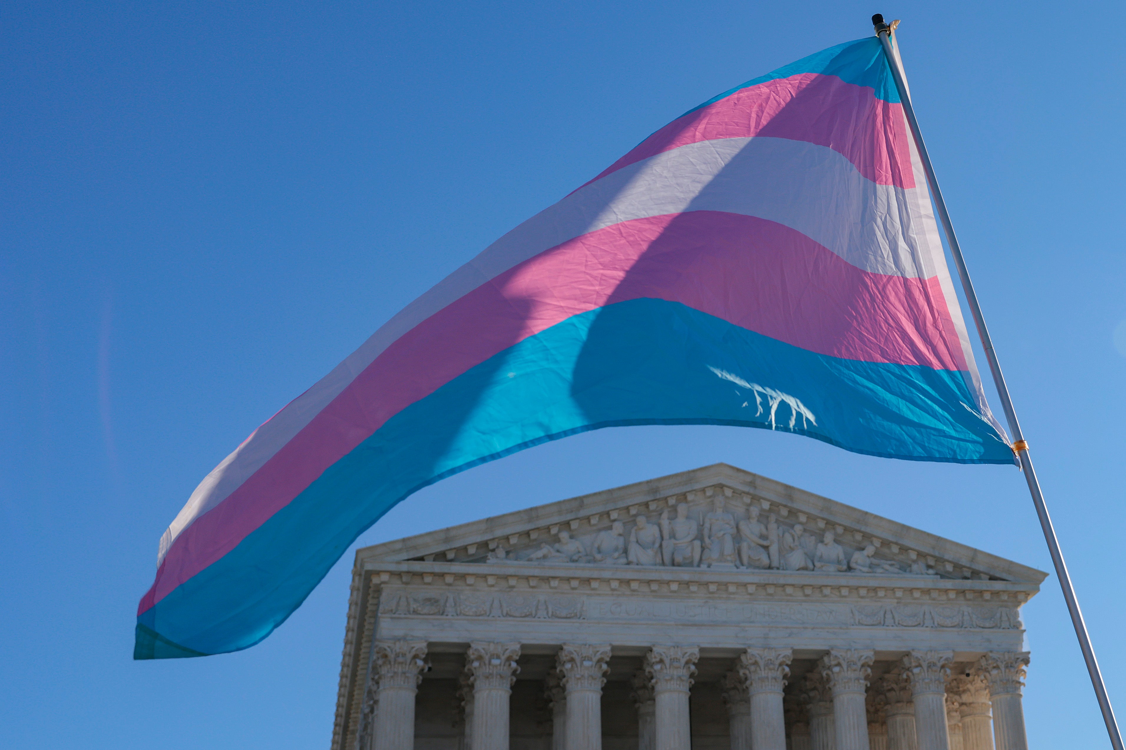 Protesters supporting transgender athletes competing in women's sports wave a transgender pride flag outside the Supreme Court