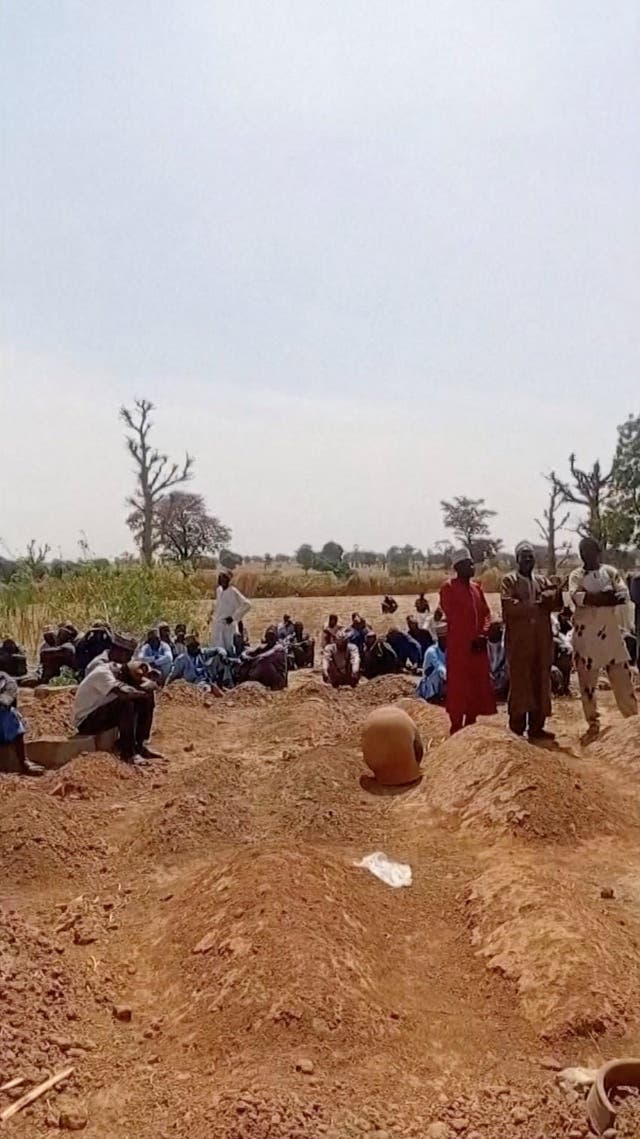 <p>People standing around graves in Nigeria following this week's attacks</p>