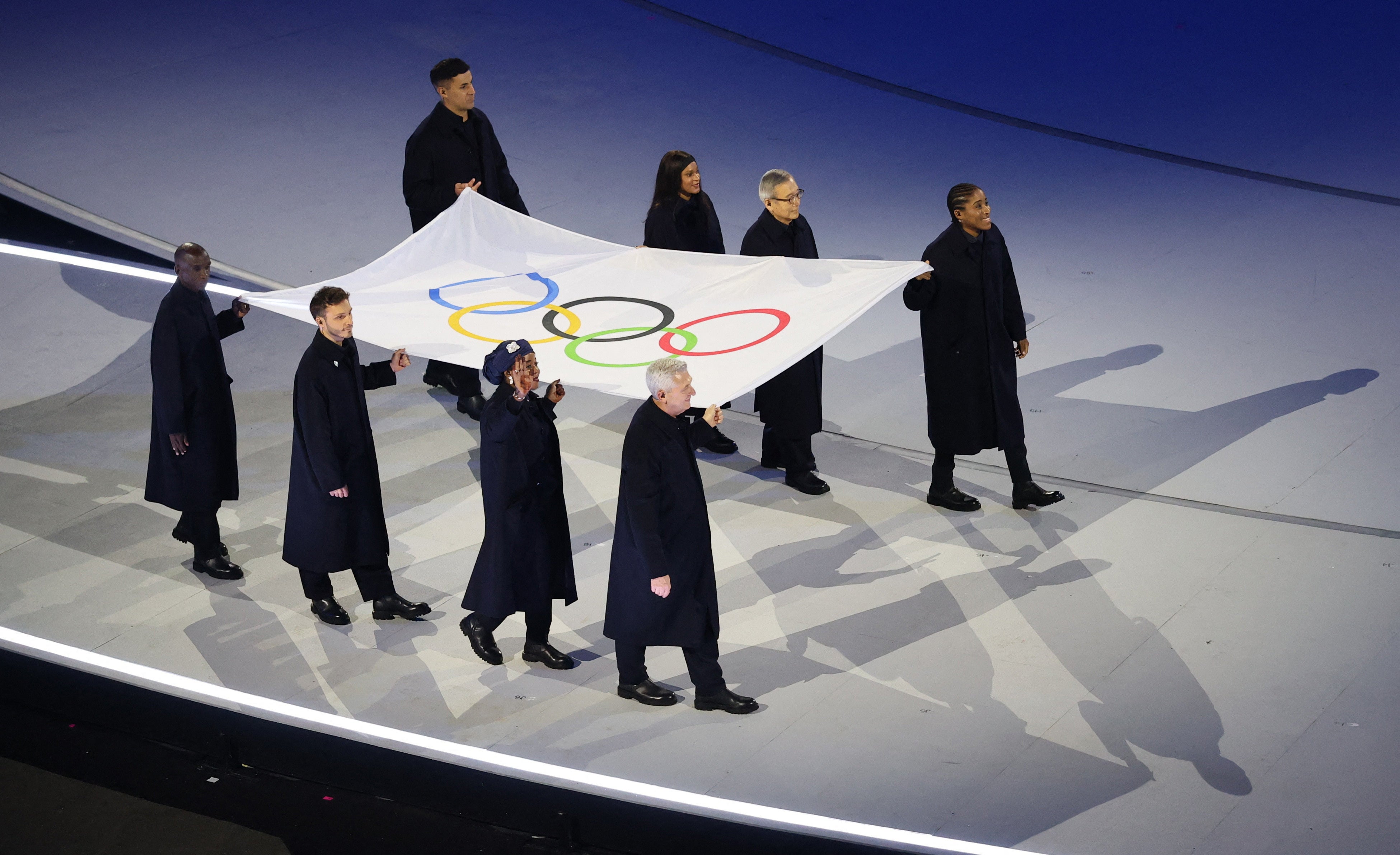 The Olympic Flag is carried by Tadatoshi Akiba, Rebeca Andrade, Maryam Bukar Hassan, Nicolo Govoni, Filippo Grandi, Eliud Kipchoge, Cindy Ngamba and Pita Taufatofua.