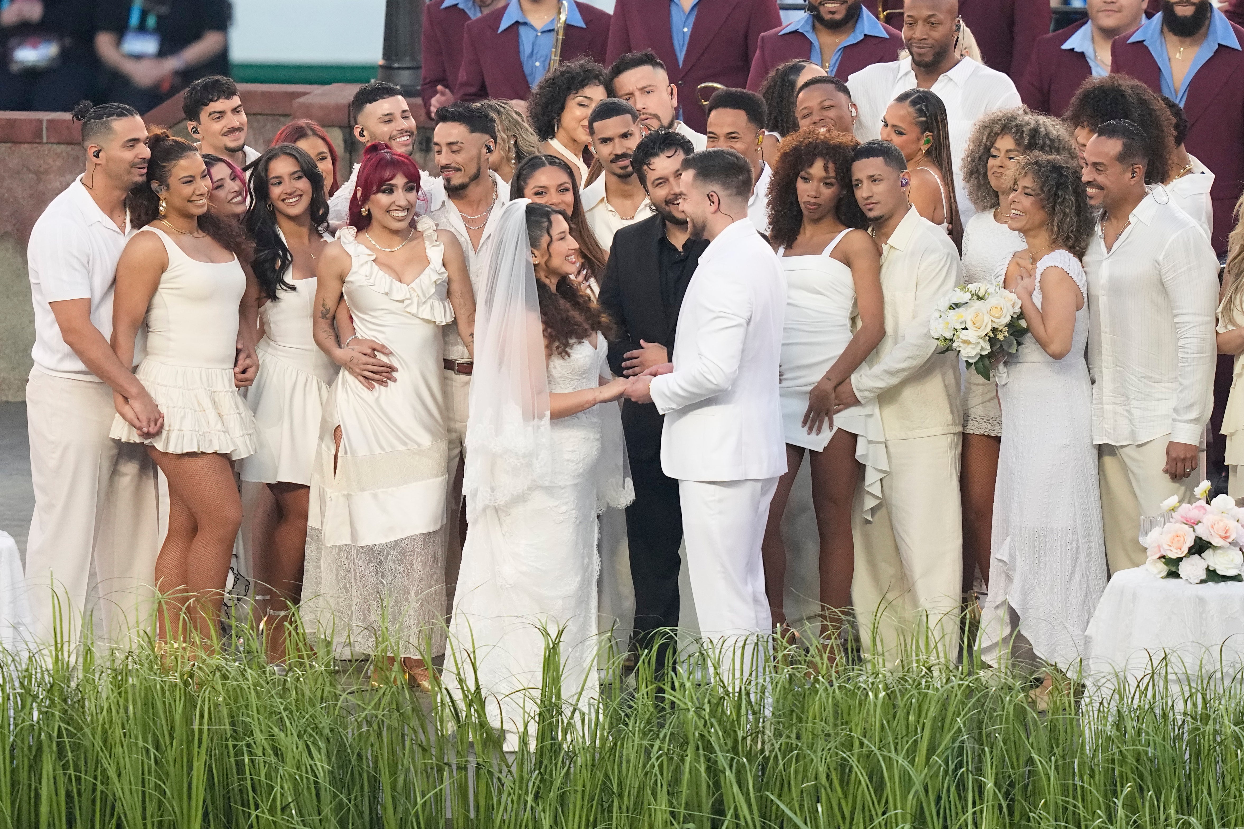 <p>Un oficiante sonriente declaró a la pareja casada, quienes, vestidos de blanco, compartieron un beso rodeados de bailarines y músicos.</p>