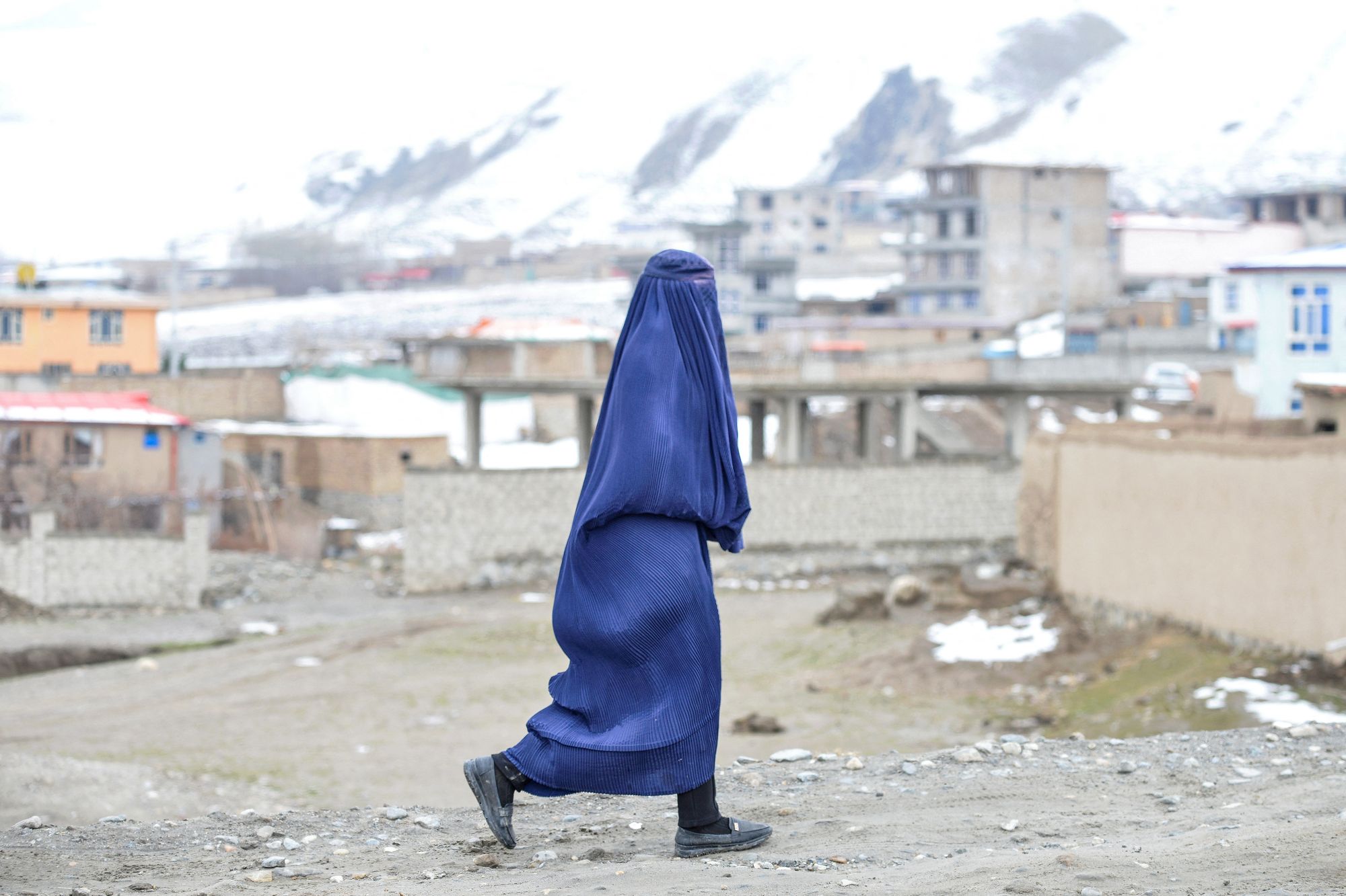 Авганистанска жена обучена у бурку шета улицом у позадини планина прекривених снегом у округу Арго у провинцији Бадакшан