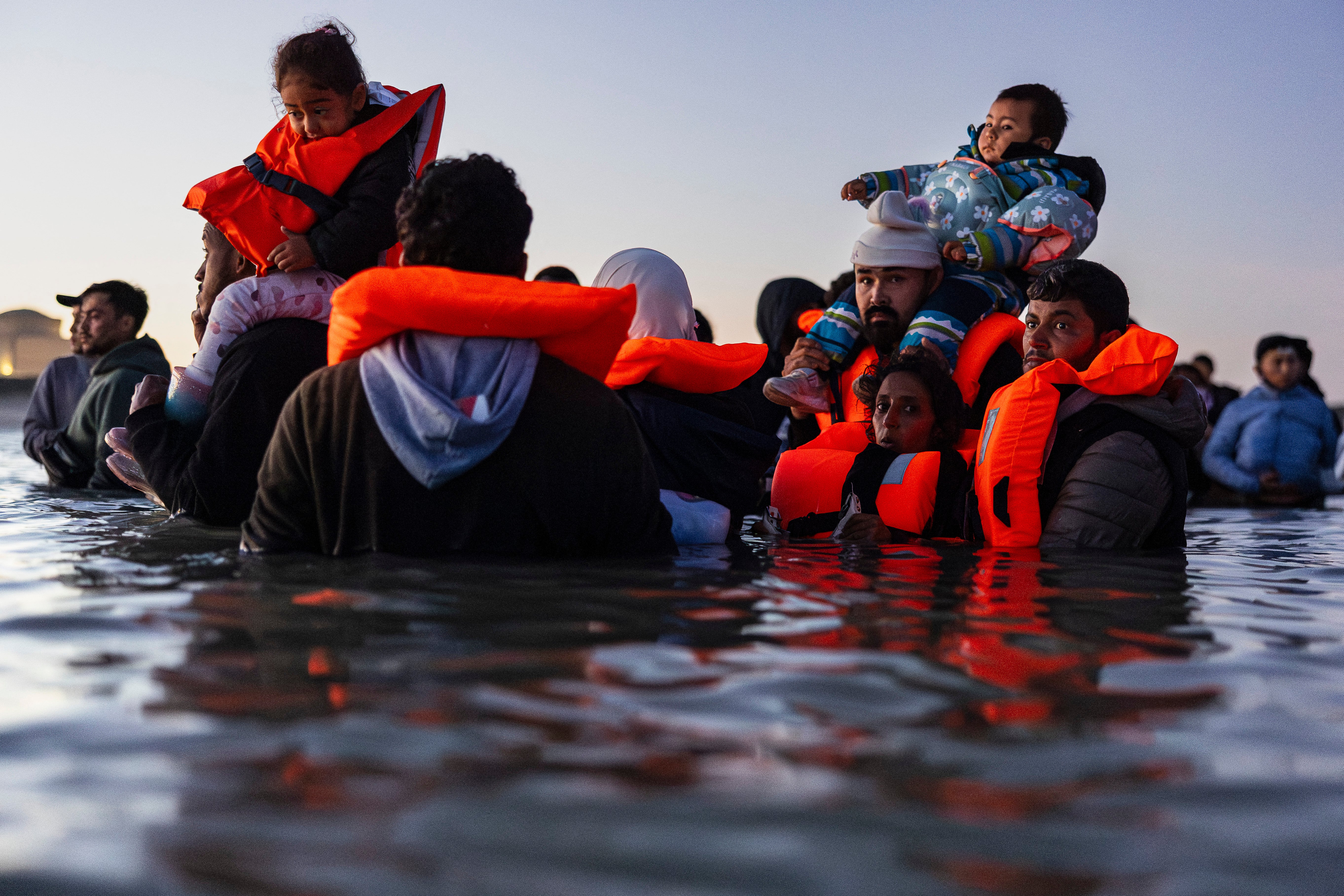 Migrants carrying children wait in the water to try to board a smuggler's boat in an attempt to cross the English Channel off the beach of Gravelines, northern France, in September 2025.