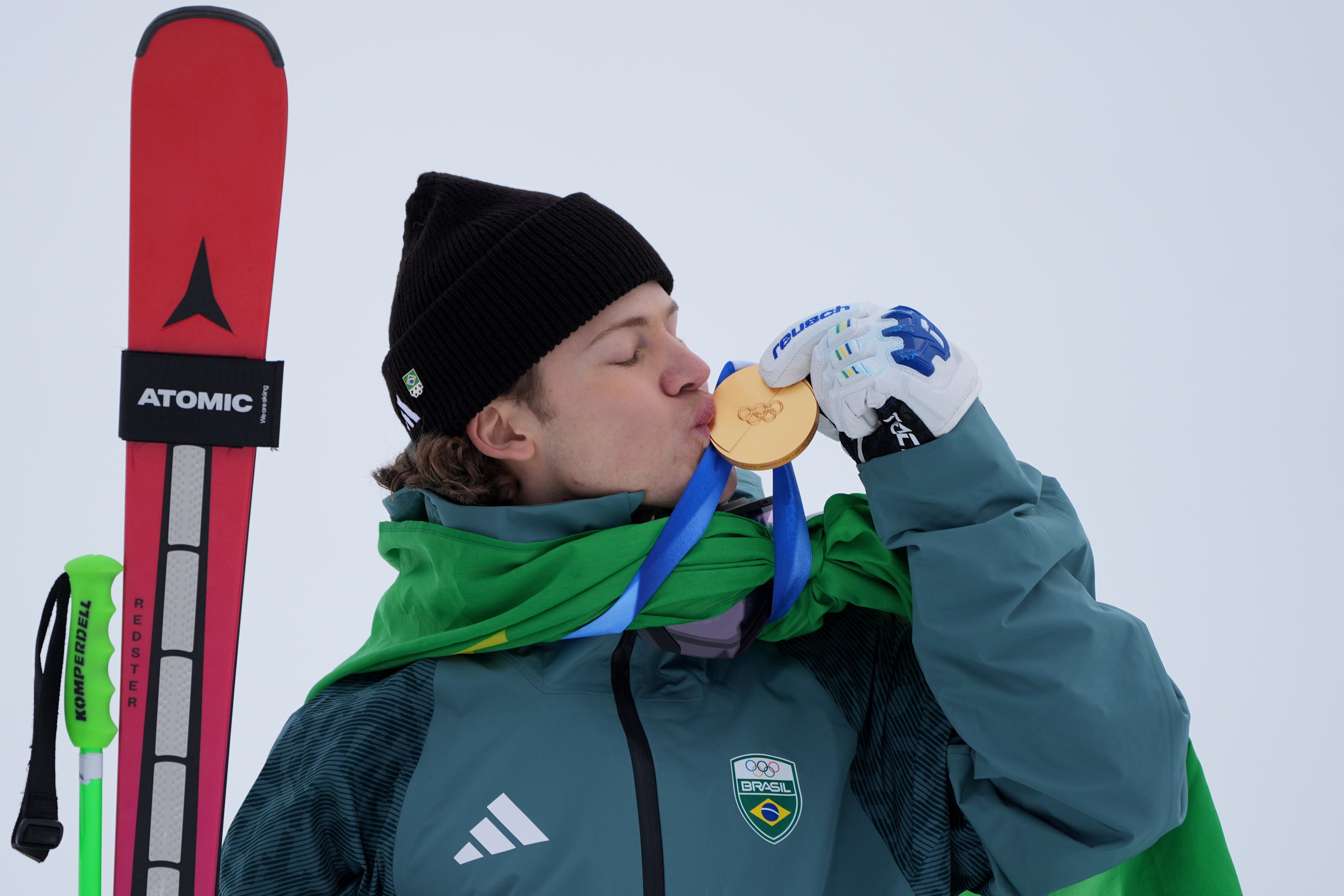 <p>Lucas Pinheiro Braathen kisses his gold medal with the Brazil flag tied around him</p>