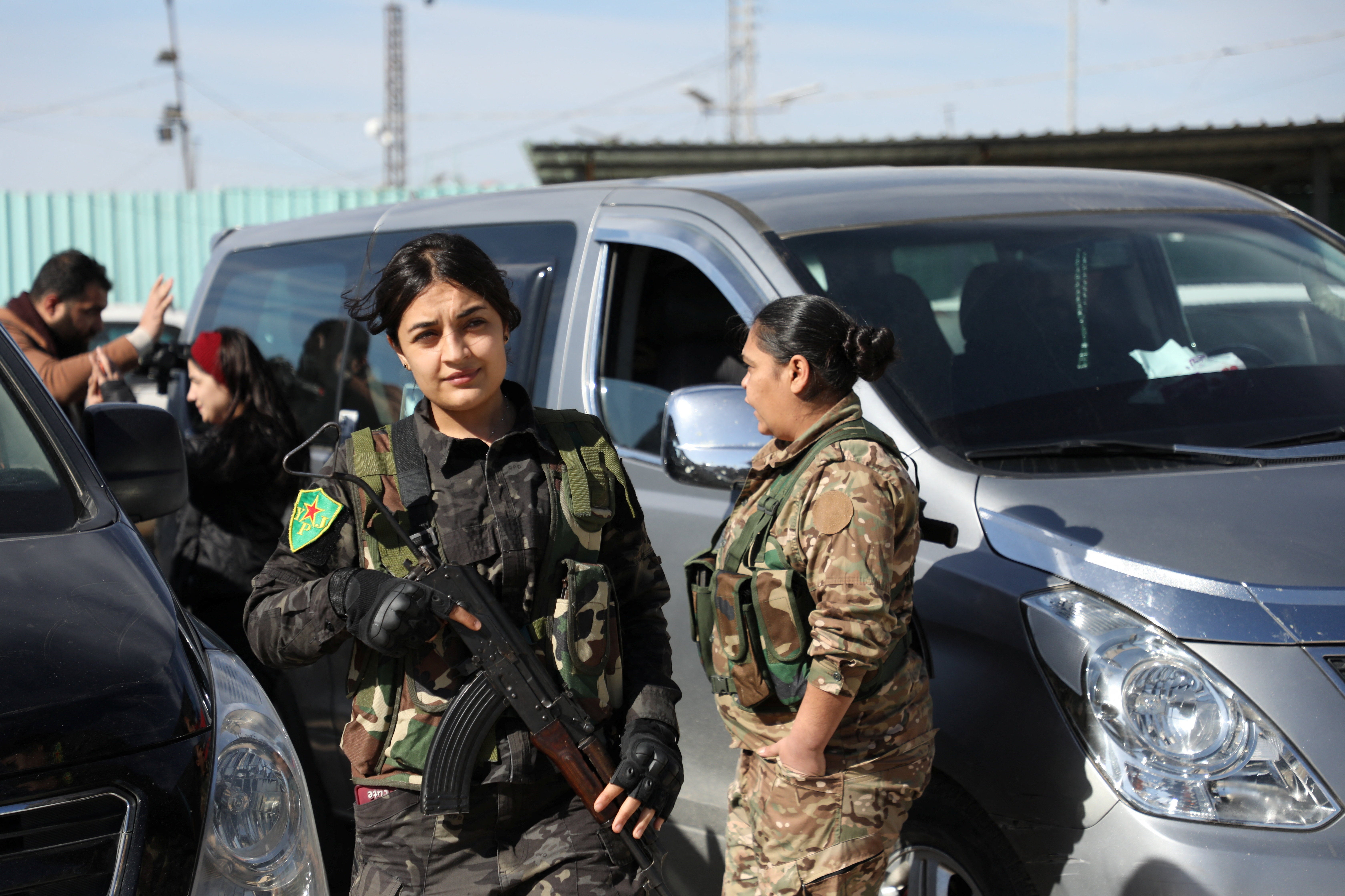 Members of Women's Protection Units of the Syrian Democratic Forces stand near camp staff members, as Australian families believed to be linked to the Islamic State militants leave Roj camp near Derik, Syria