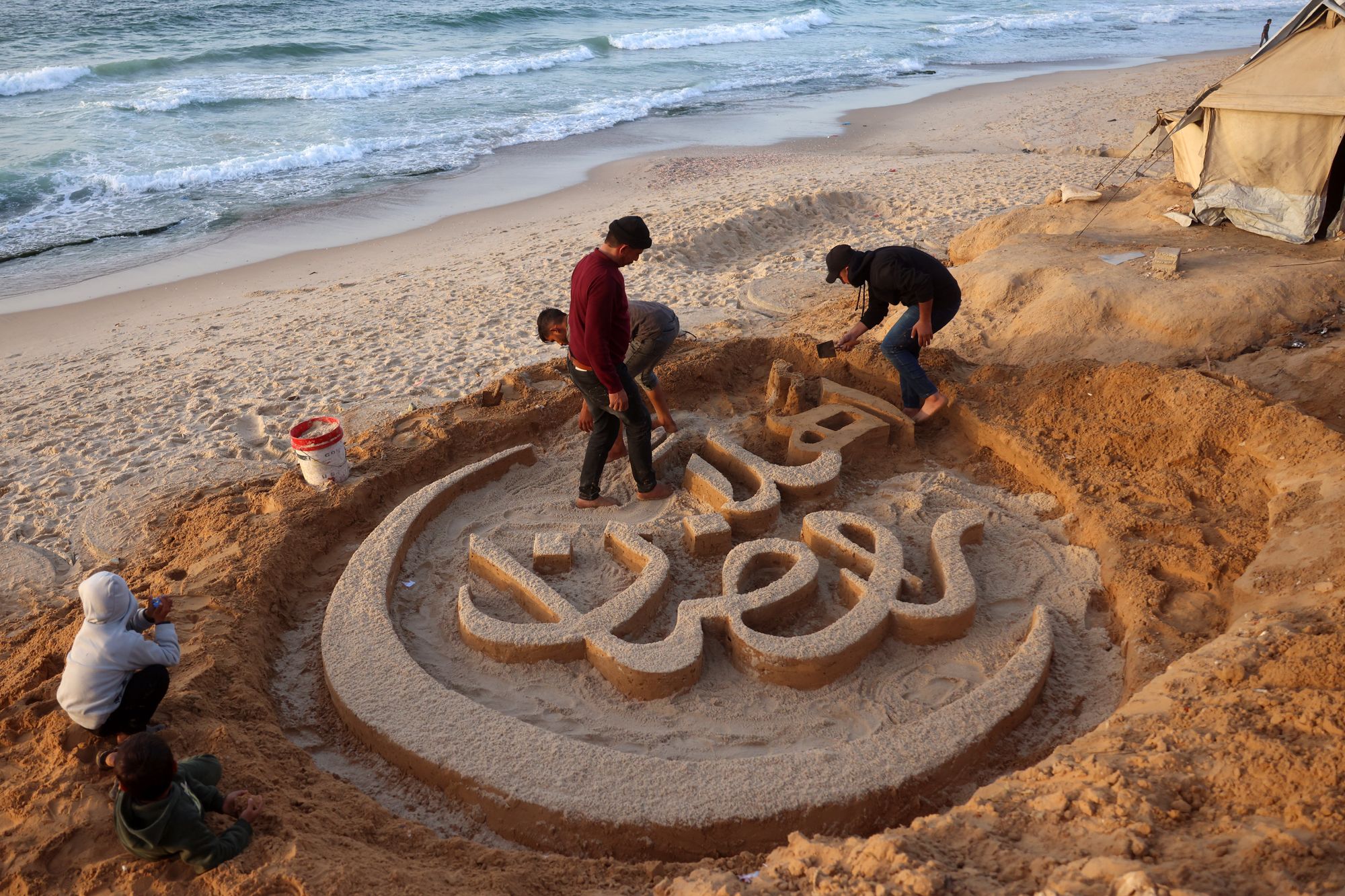 Palestinian artist Yazeed Abu Jarad creates a sand sculpture displaying the message ‘Welcome Ramadan’ in Khan Younis