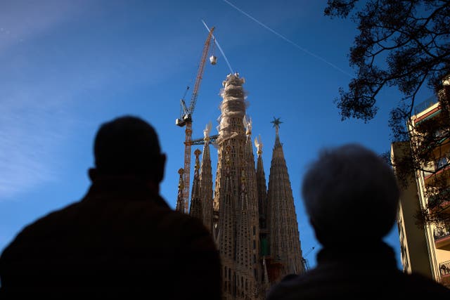 <p>People watch as a crane lifts the upper arm of the cross onto the Tower of Jesus Christ at the Sagrada Familia in Barcelona, Spain.</p>