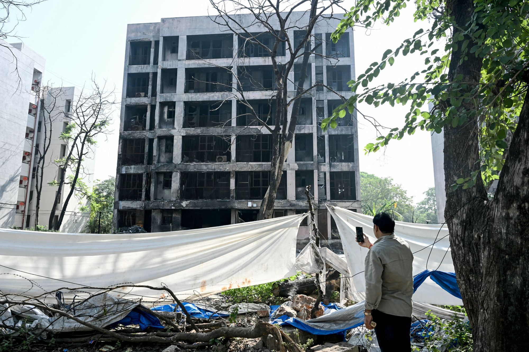A man takes photos of a charred building at the crash site of Air India flight AI171 in Ahmedabad