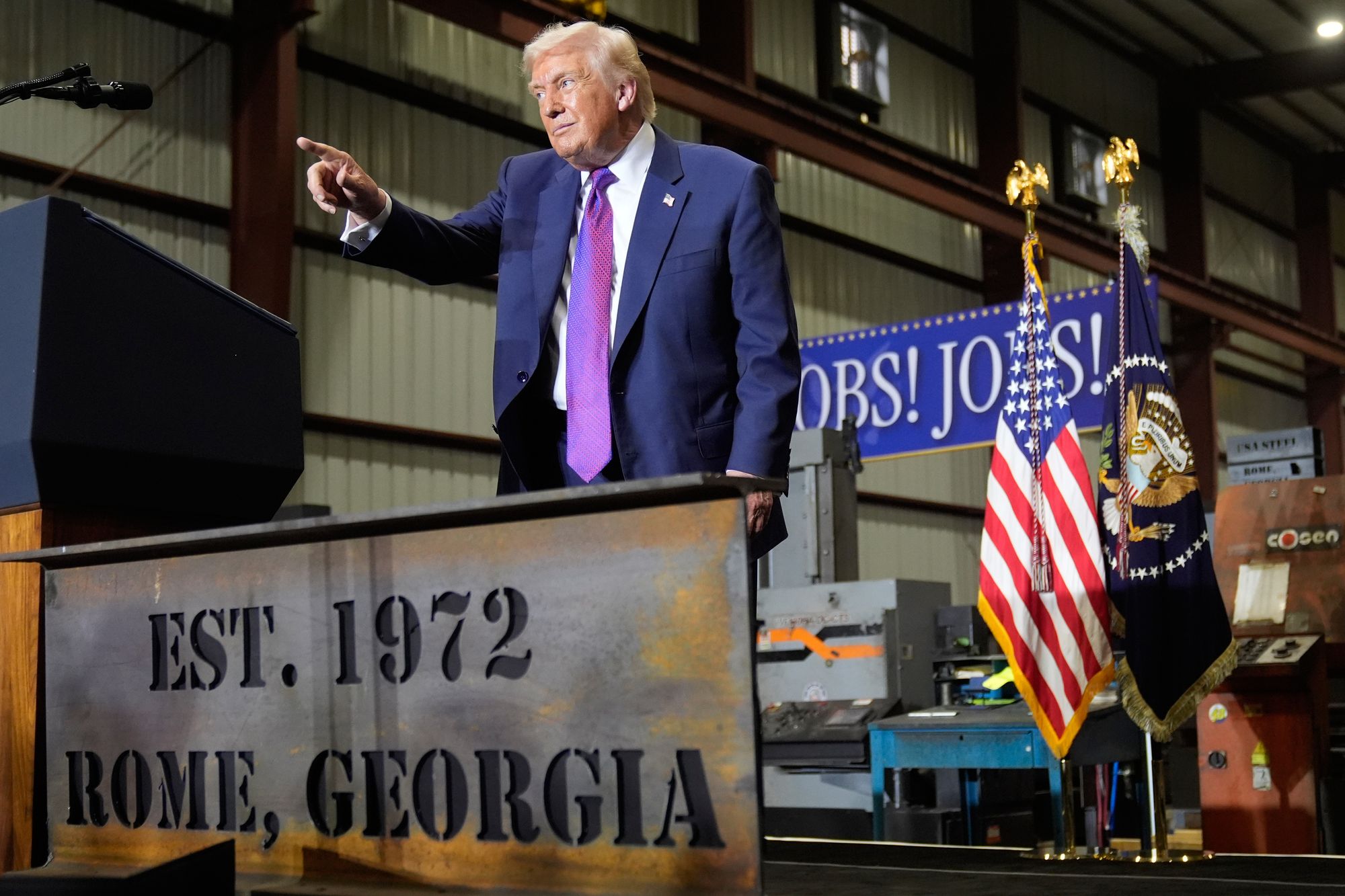 The President in front of a banner reading “Jobs! Jobs! Jobs!”
