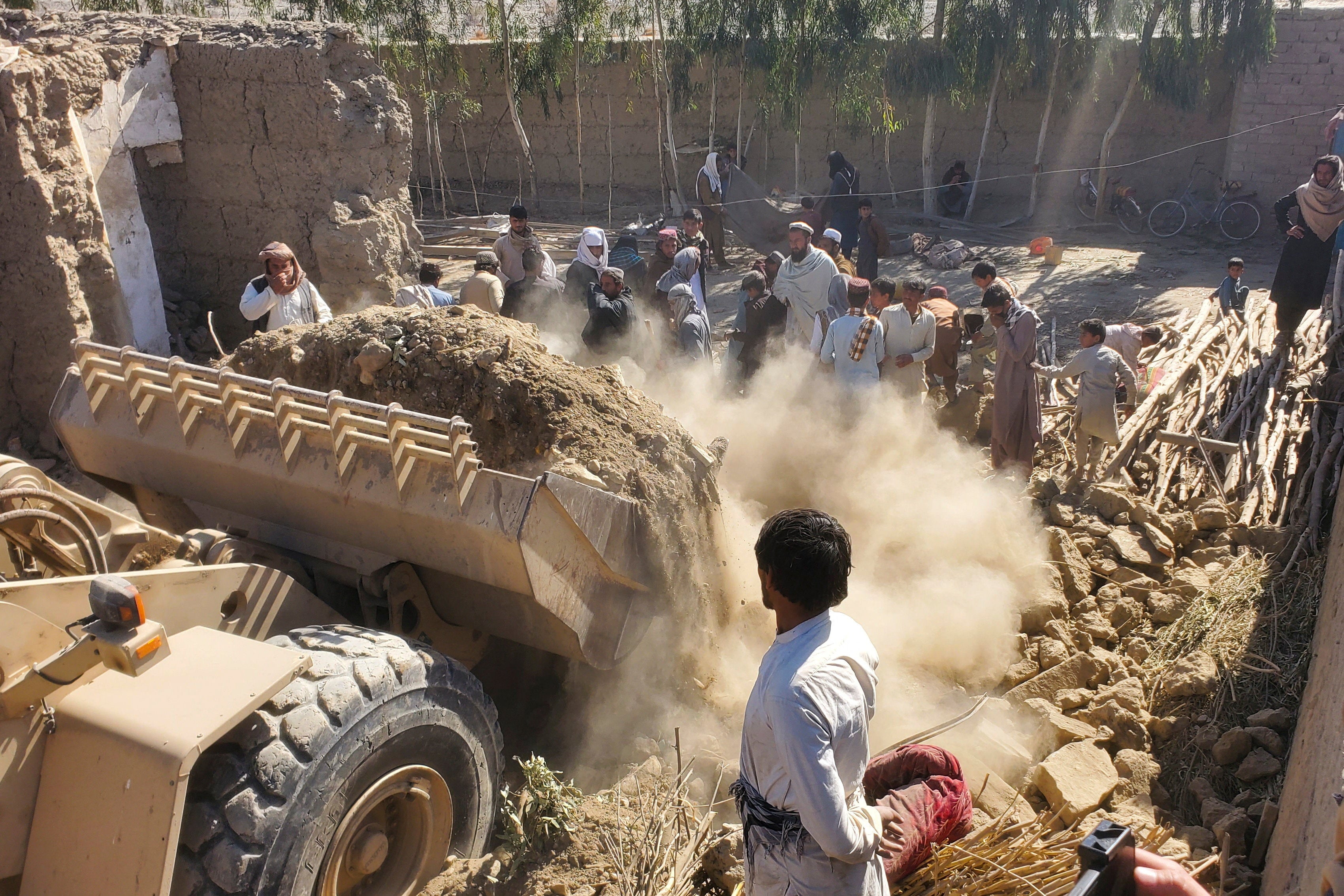 Residents gather as machinery clears the debris of a damaged house, following the Pakistani air strikes, in Nangarhar, Afghanistan