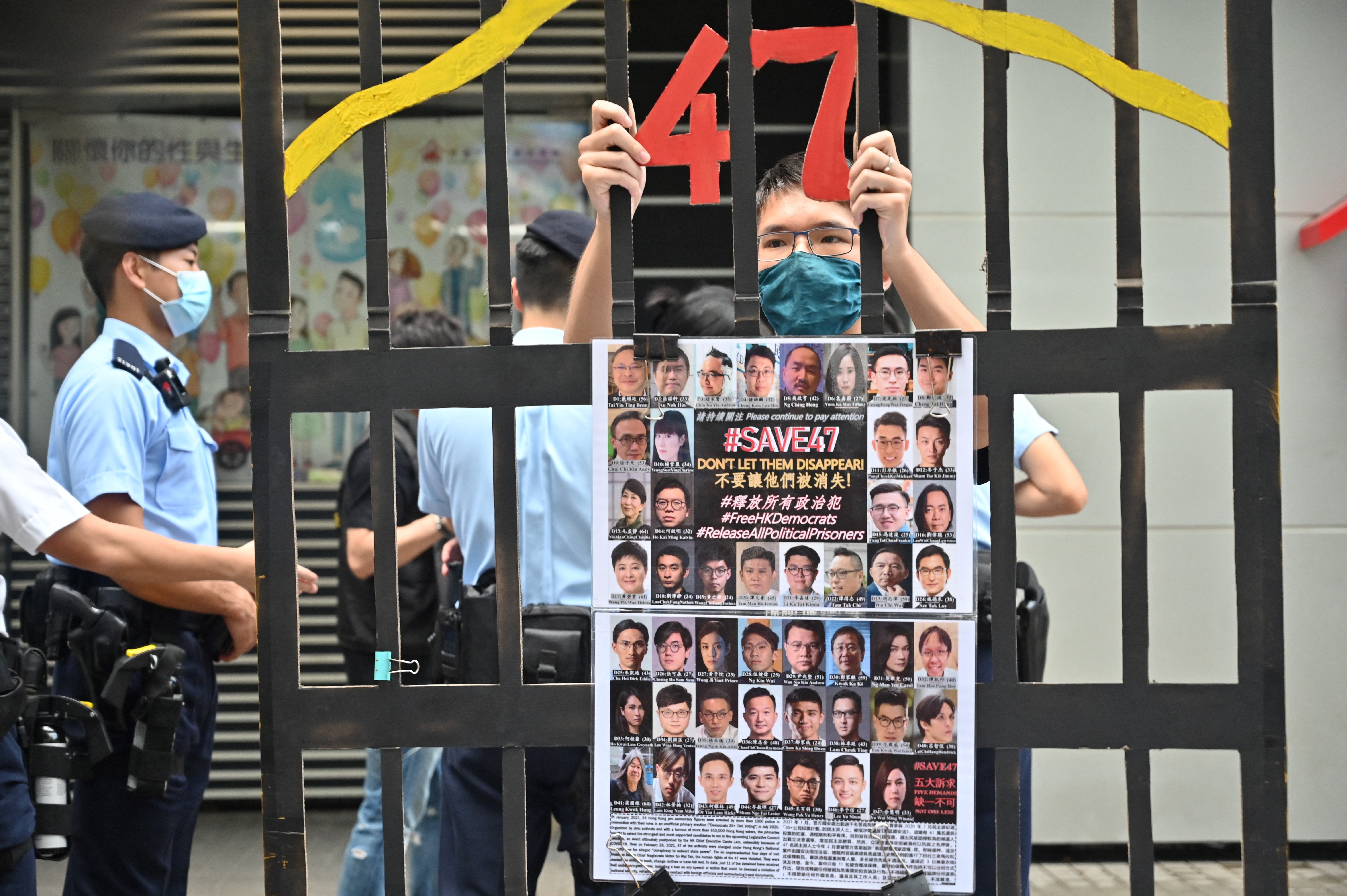 <p>File: A protester stands behind a mock jail with photos of the 47 pro-democracy figures already in prison</p>